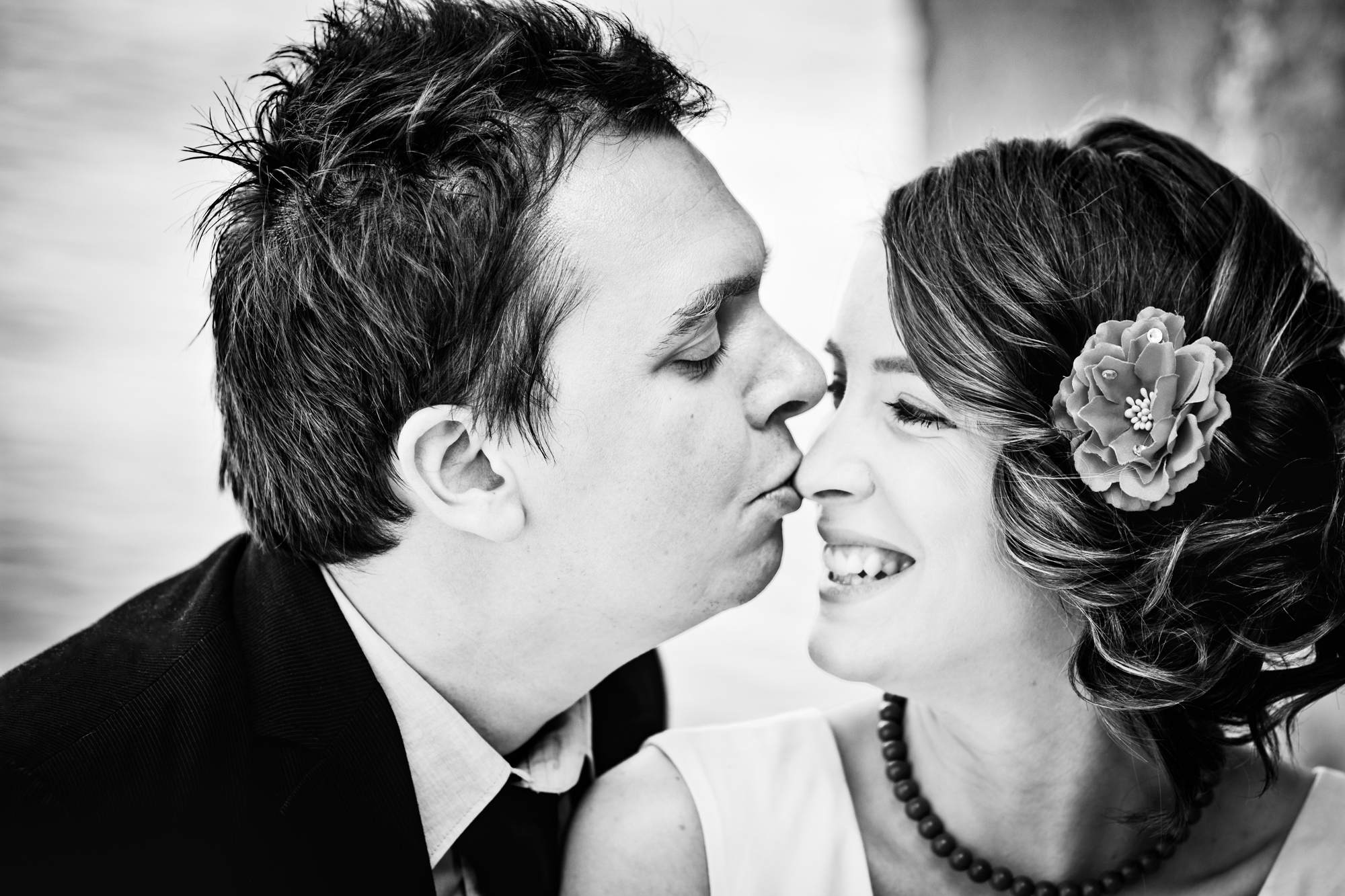 Couple share a close kiss, smiling during an intimate black and white engagement session.