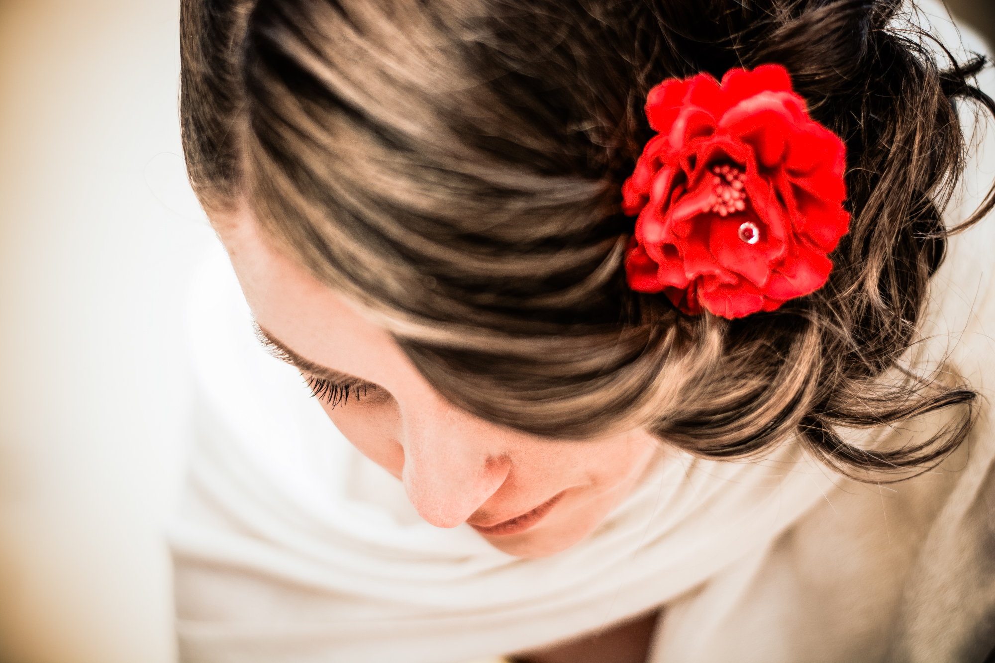 Close up of bride’s hairstyle with red flower accessory and soft natural light.