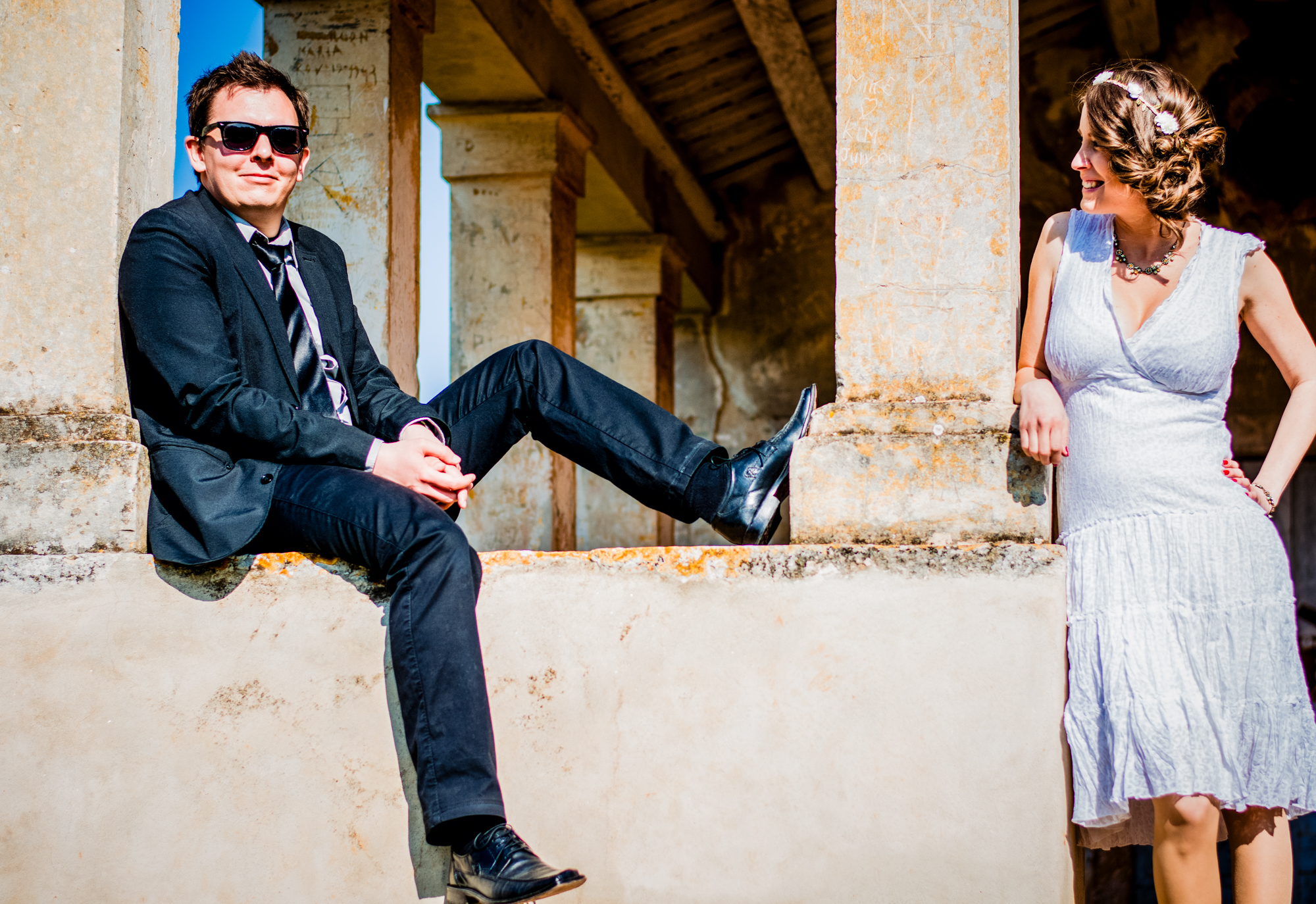 Couple pose apart on stone balcony, laughing during relaxed Rovinj engagement session.