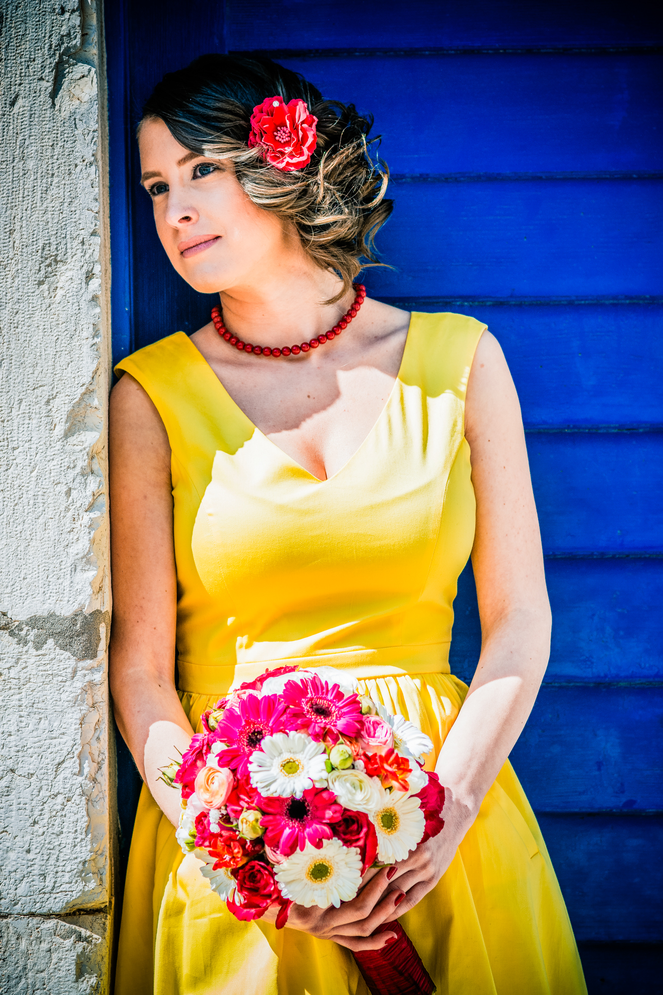 Woman in yellow dress leans against bright blue door holding bouquet in Rovinj old town.