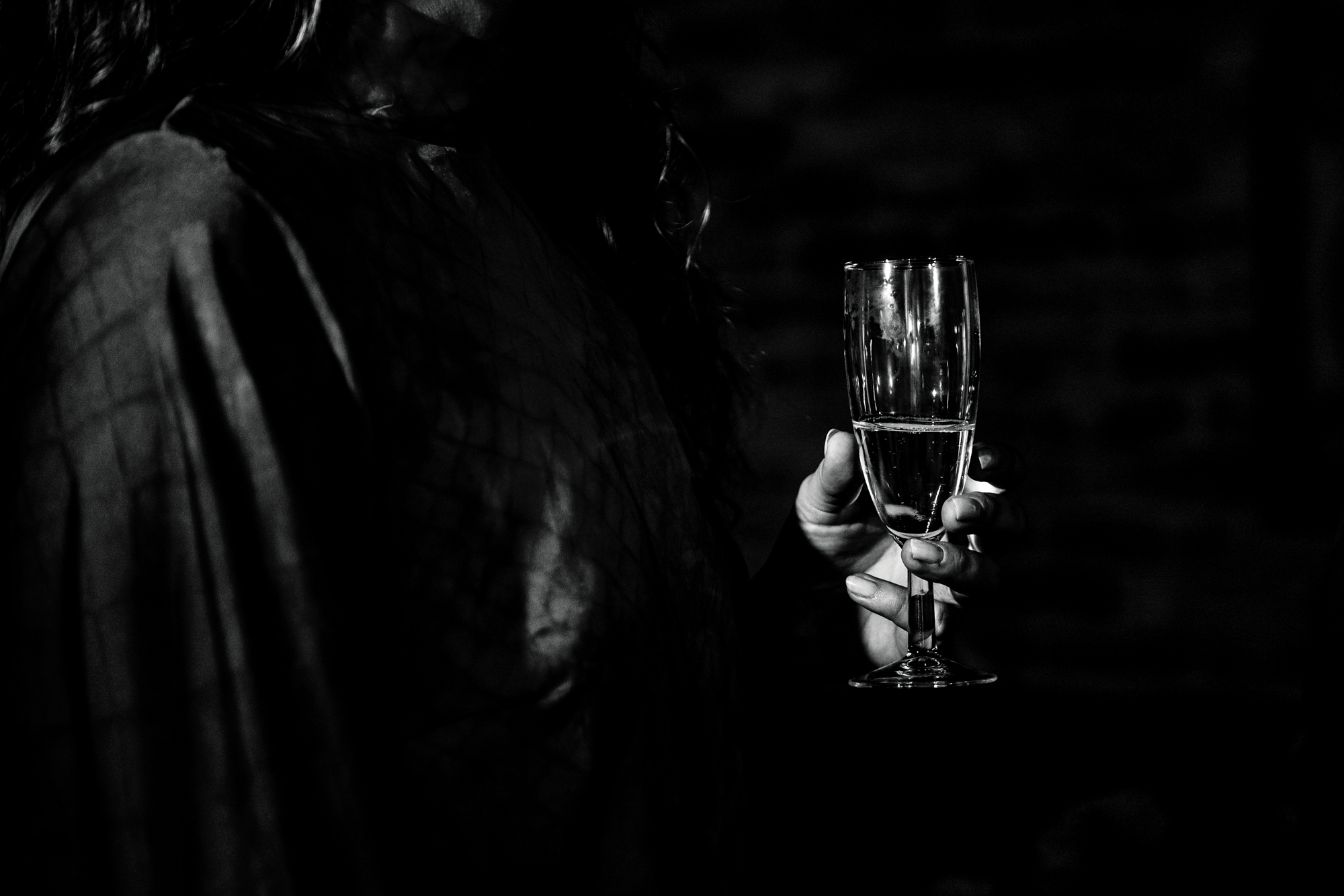 Close-up of champagne glass held in hand during the dark, atmospheric wedding reception.