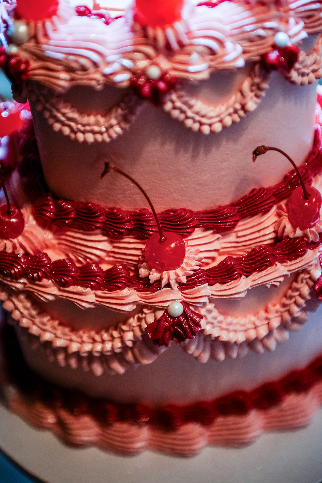Close-up of pink wedding cake piping and cherries during the rockabilly wedding party.
