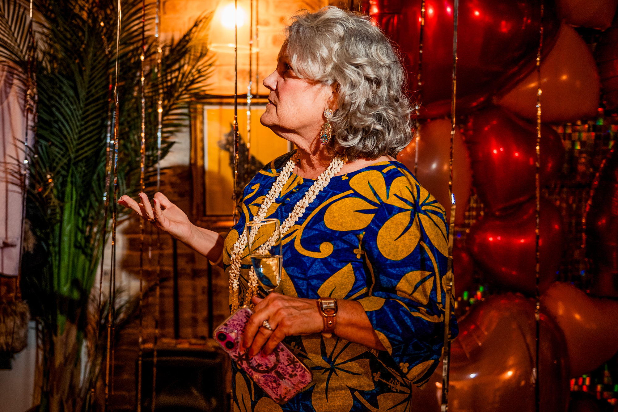 Older guest holding a drink beside heart balloons during the wedding party at Racks Bristol.