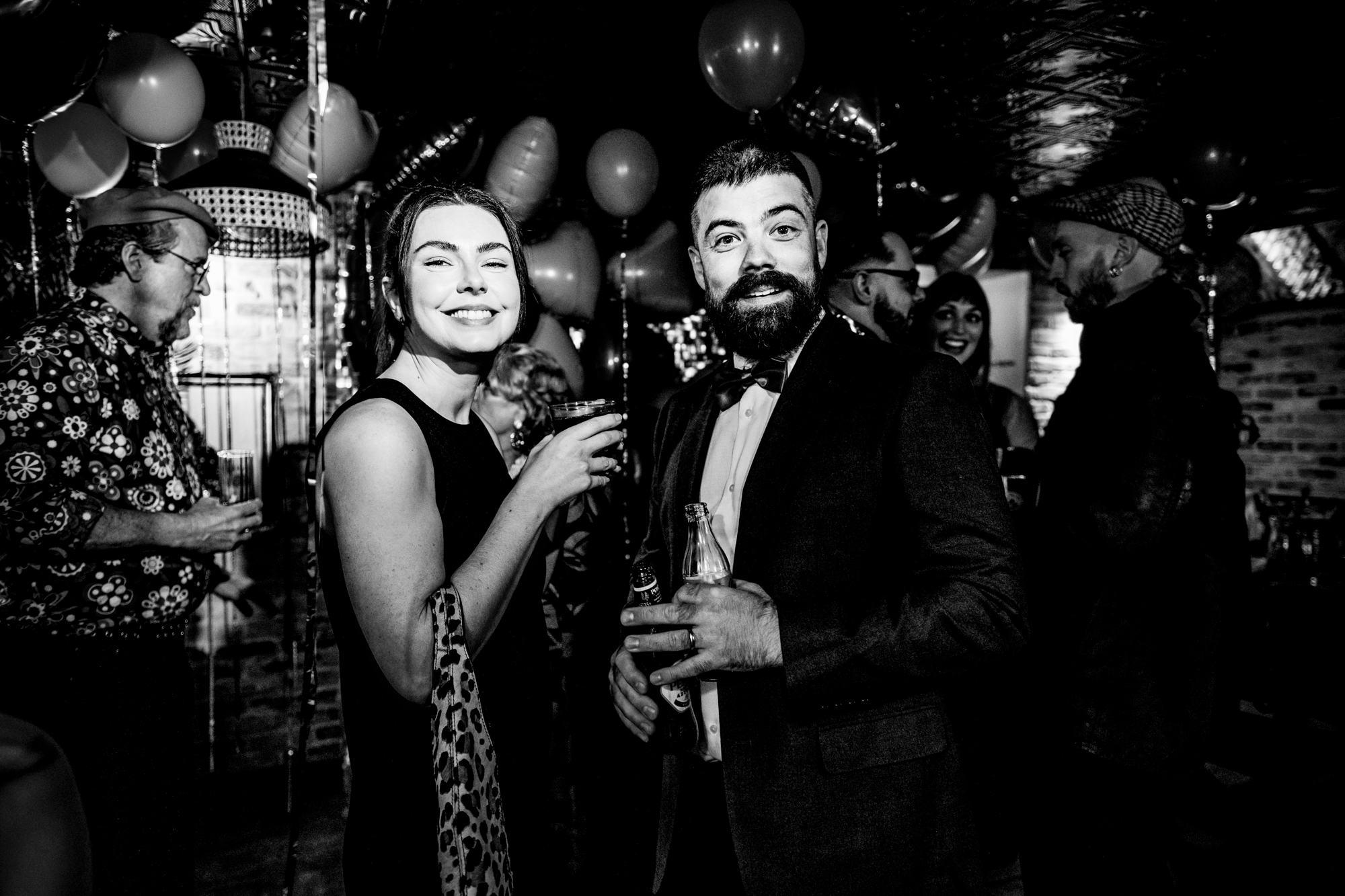 Two guests smiling with drinks during the evening wedding party.