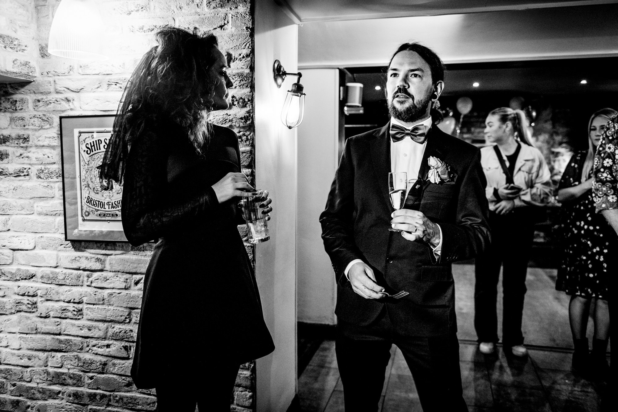 Groom in a tuxedo holding champagne while chatting in the Playroom at Racks Bristol.