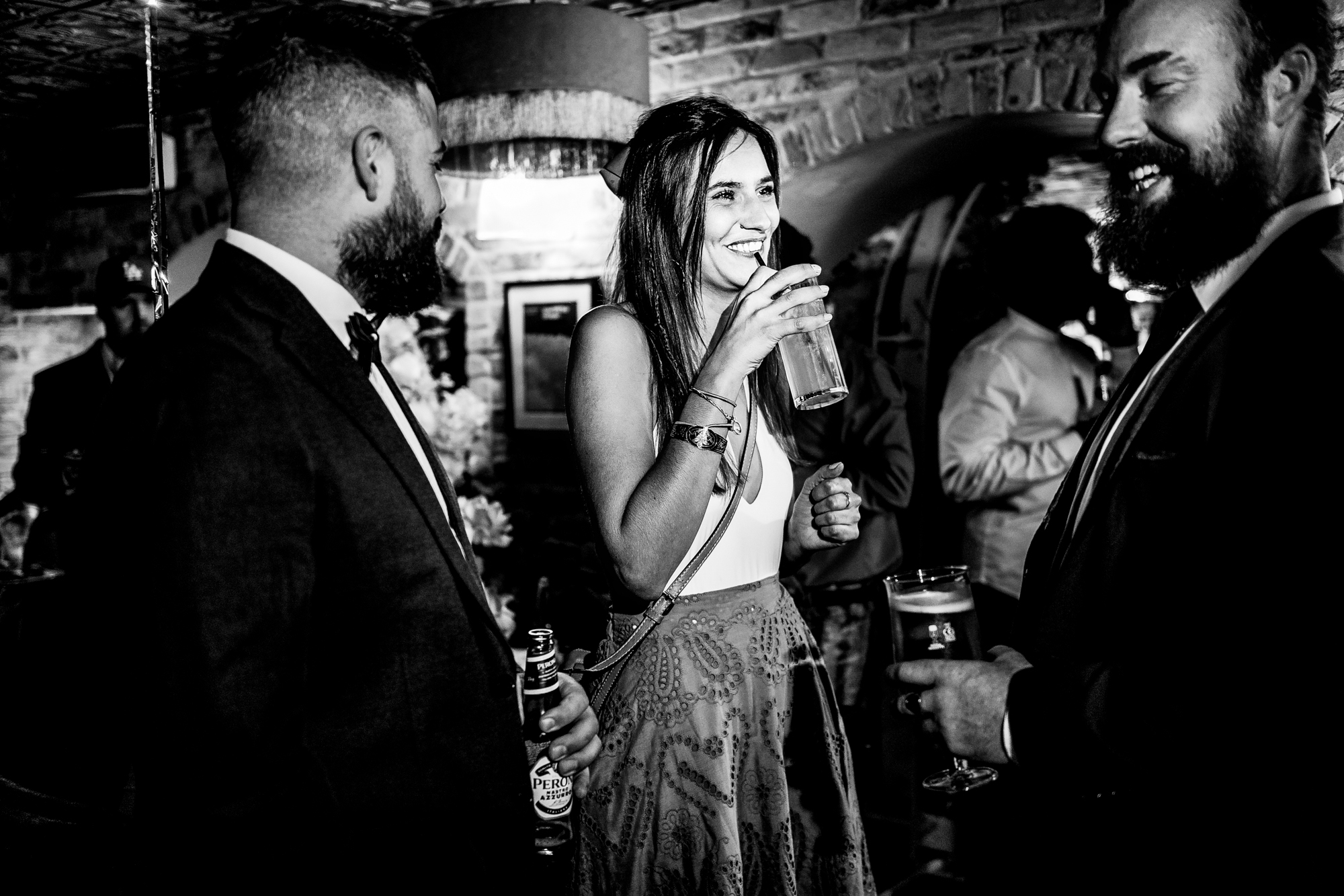 Three guests laughing together with drinks in black and white at the reception.