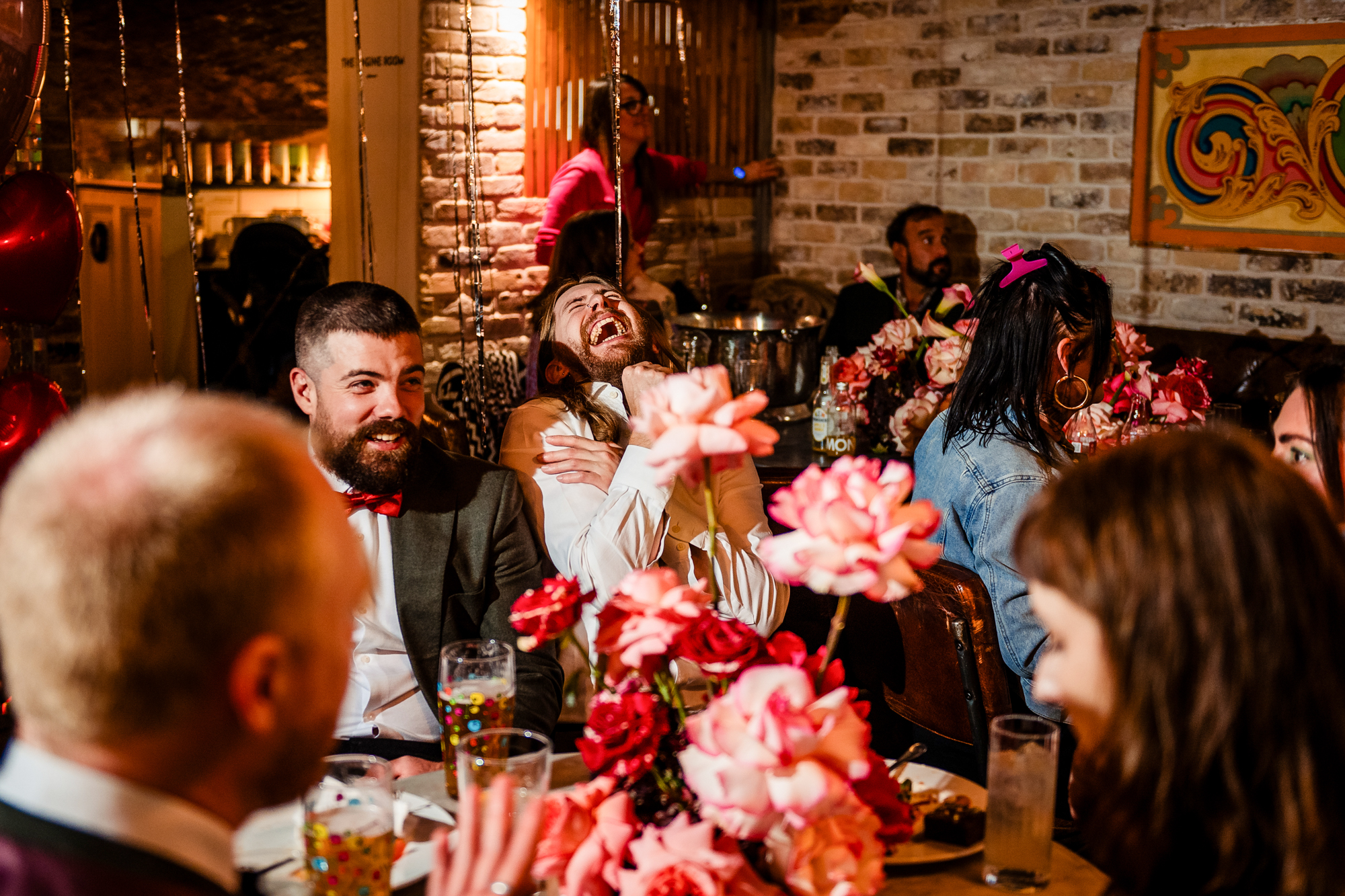 Guests laughing around a flower-filled table during the lively wedding party at Racks Bristol.