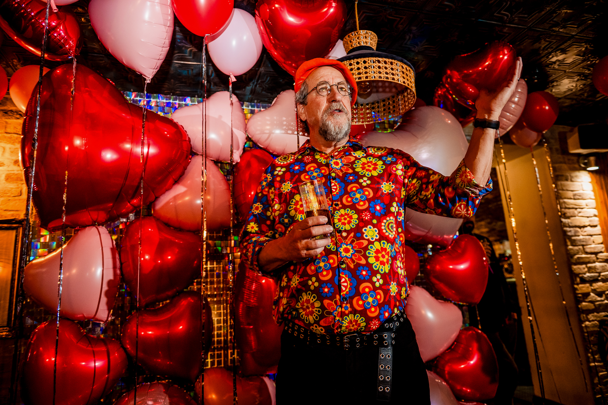 Older guest in a floral shirt speaking beside the balloon backdrop at Racks Bristol.