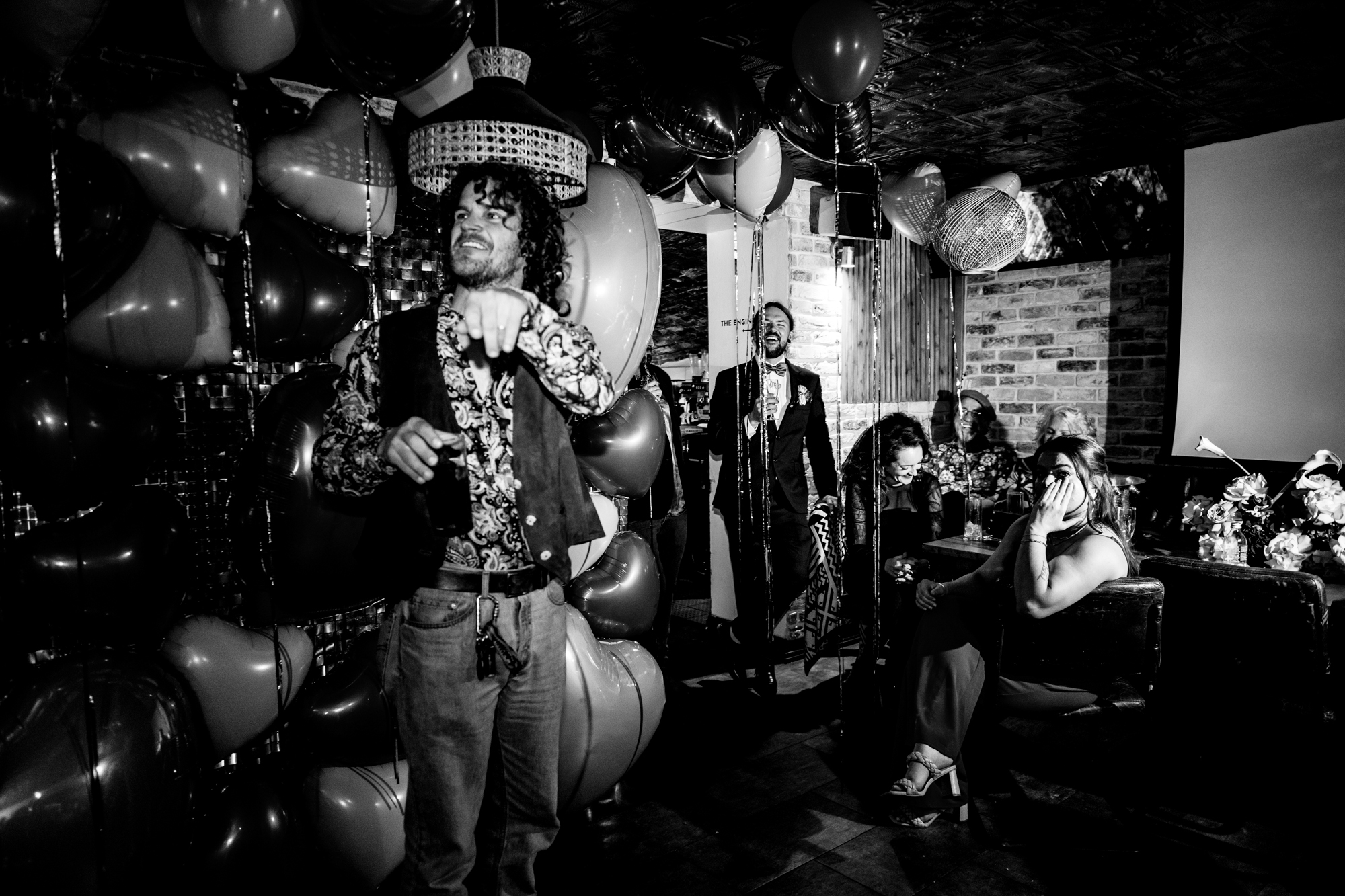 Guest points across the room as friends laugh during speeches at Racks Bristol.