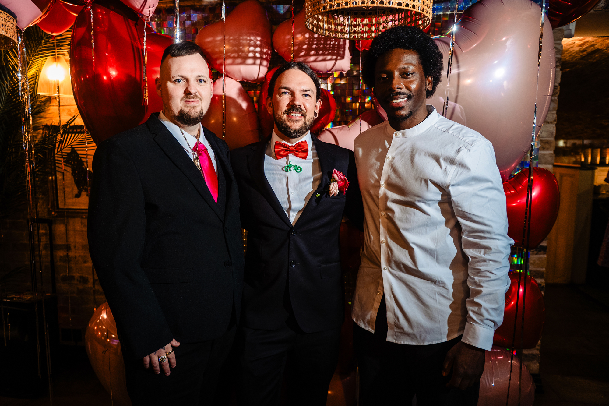 Guests with the groom stand together in front of heart balloons at Racks Bristol.