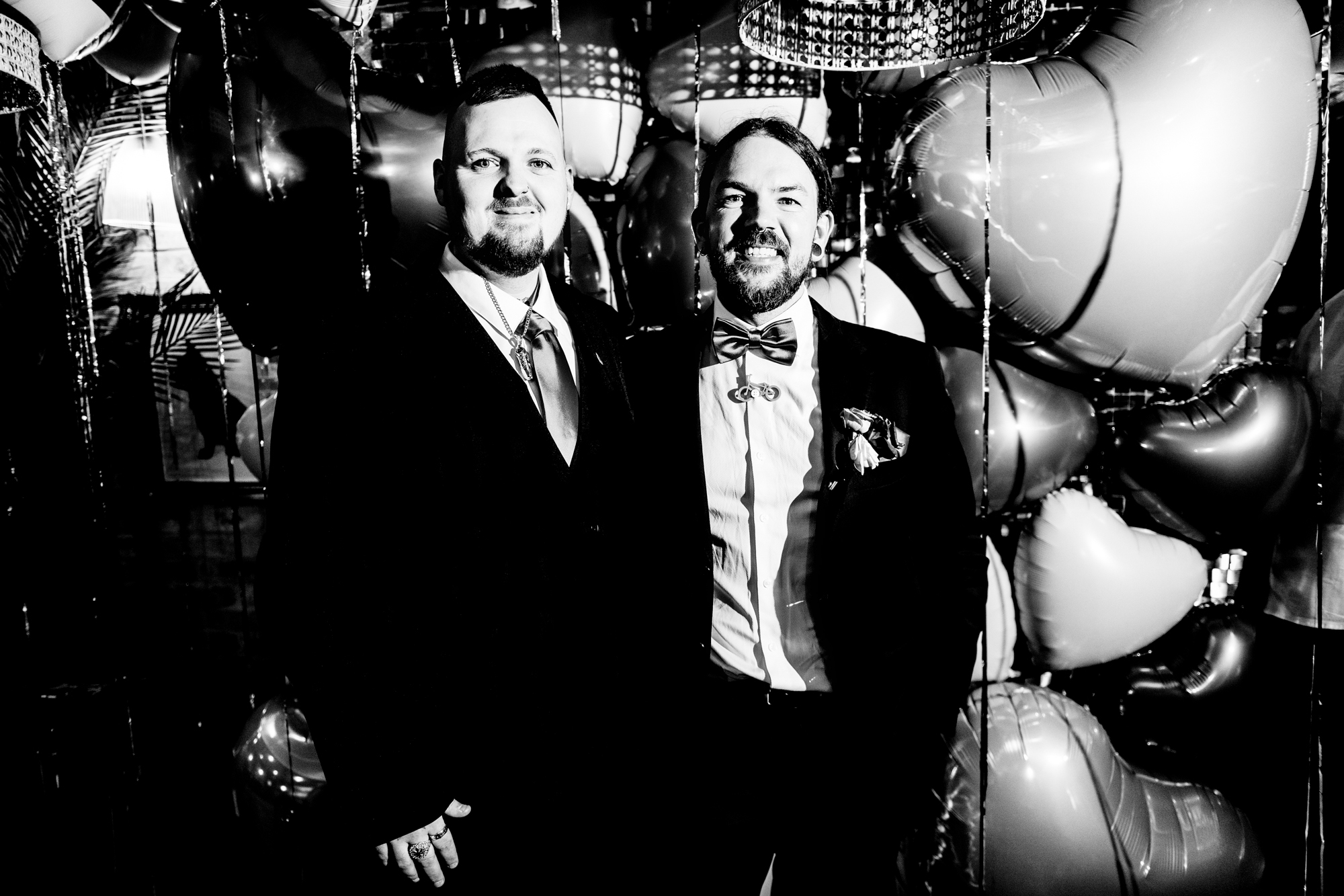 Groom and a guest smile in front of the balloon backdrop.