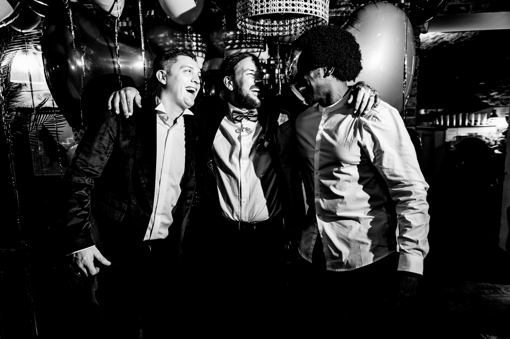 Guests with the groom laugh together beneath the heart balloons.