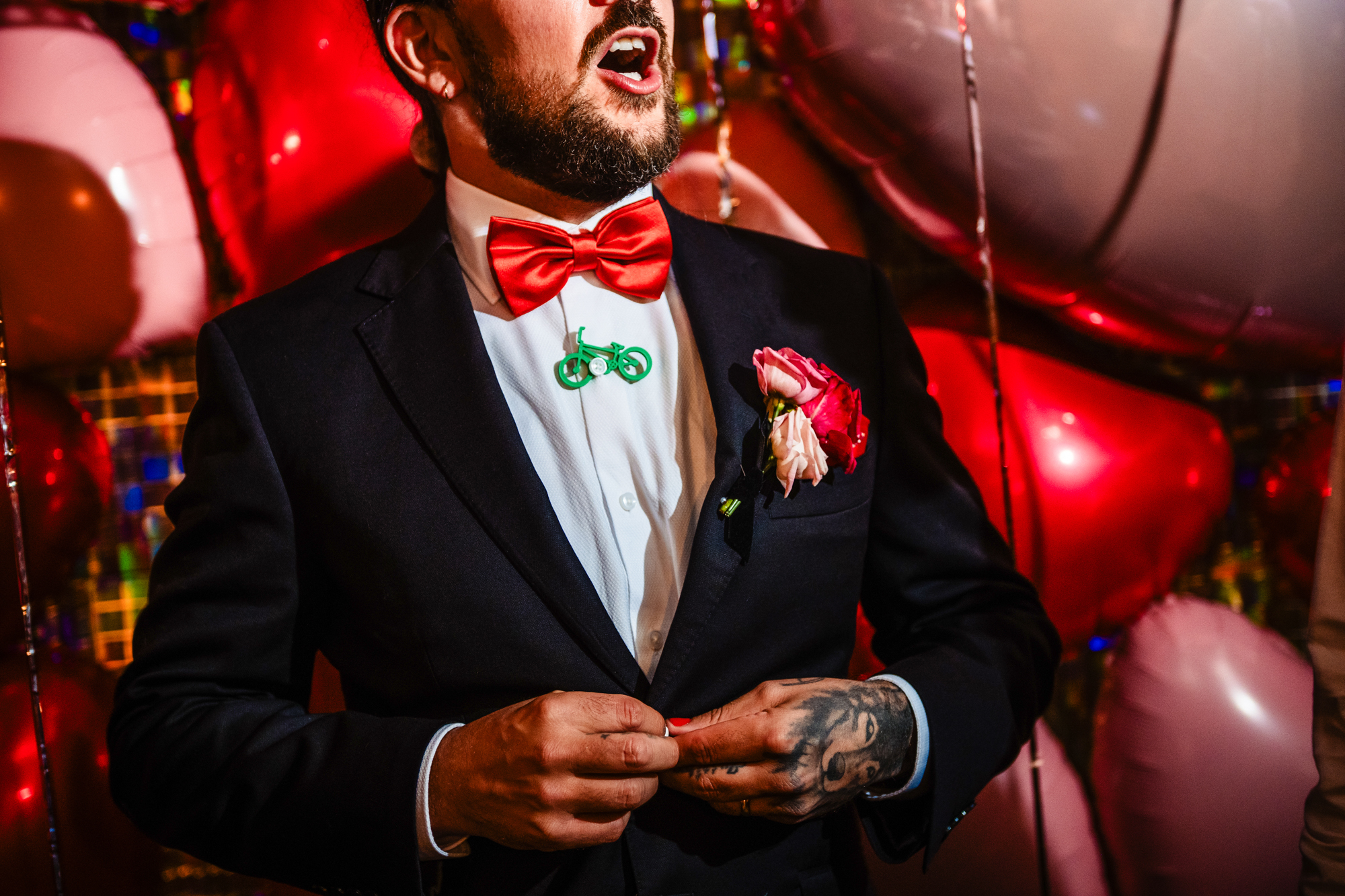 Close-up of the groom in a tuxedo with red bow tie and rose boutonniere.