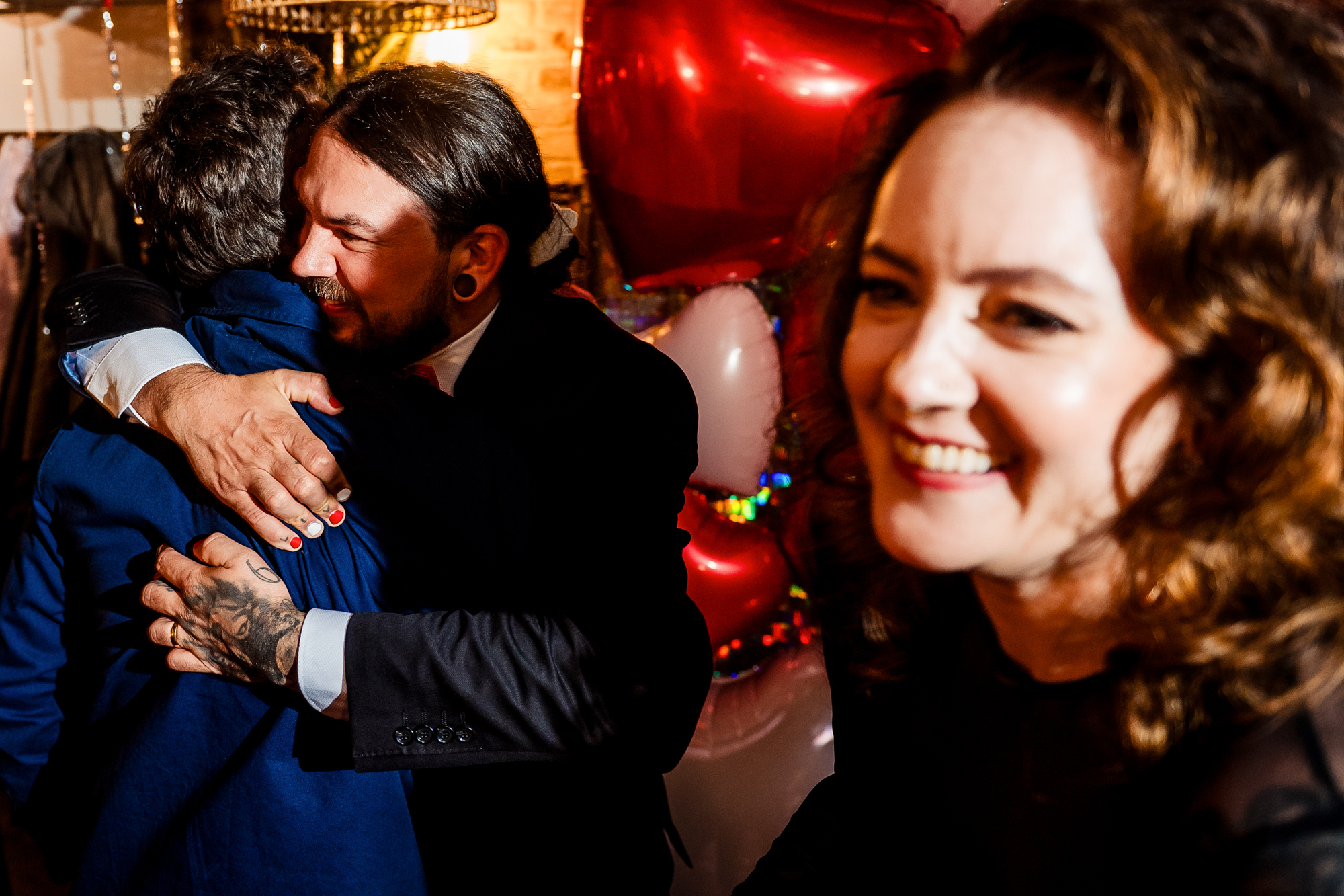 Guests embrace warmly during the wedding party as the bride smiles nearby.