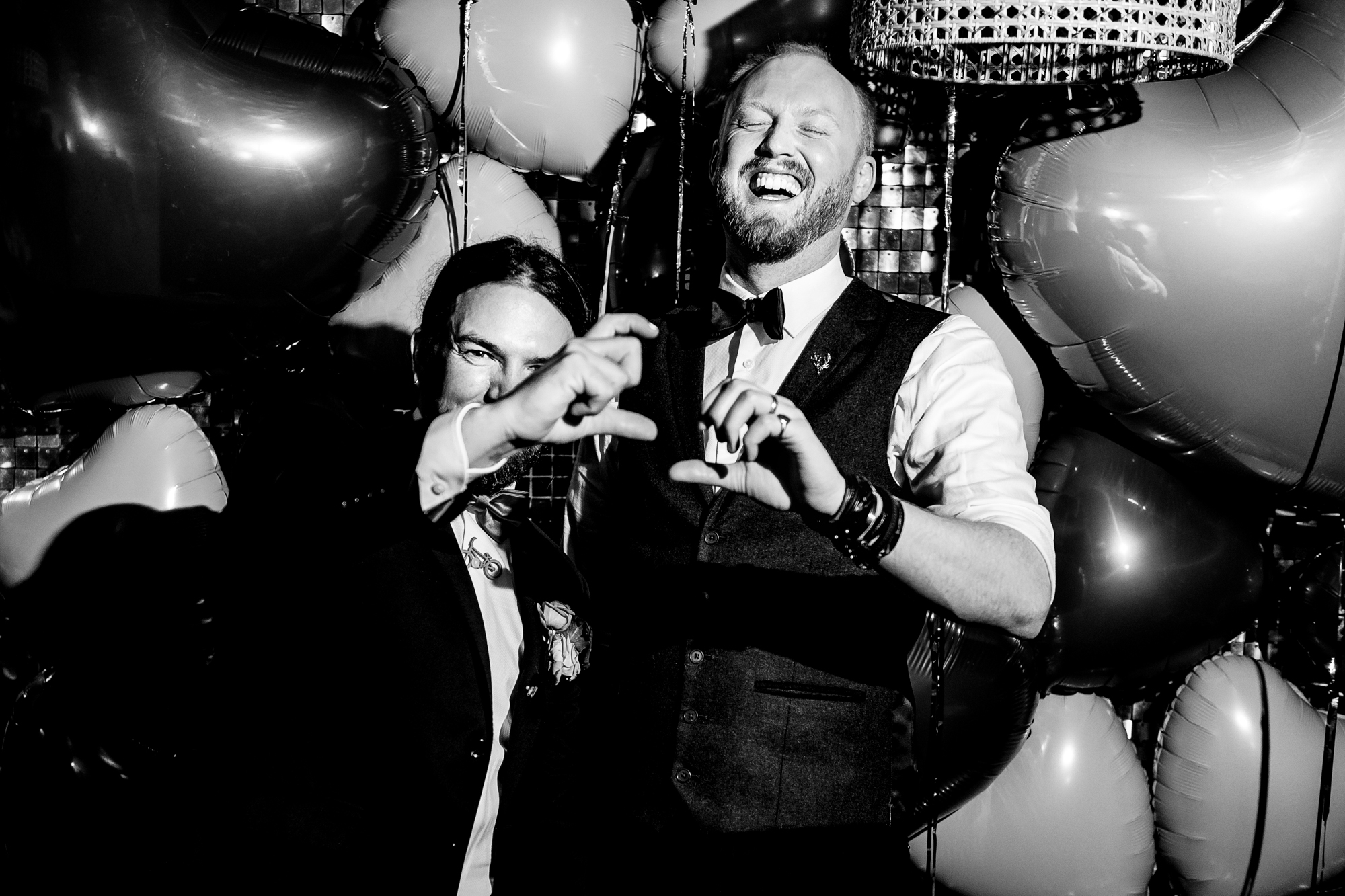 Bride and a wedding guest laugh with hand gestures beneath the balloons.