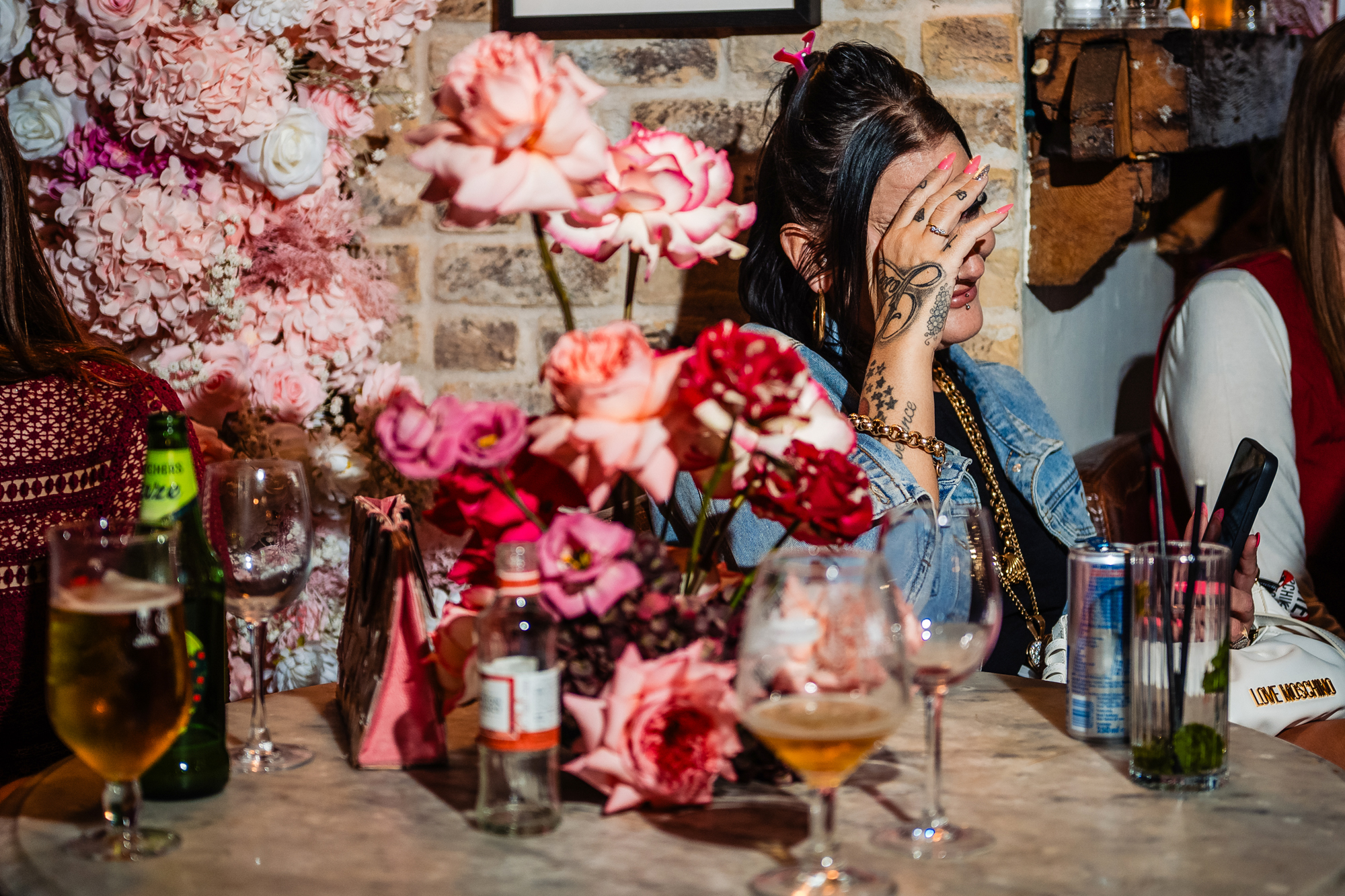 Guest covers her face beside pink flowers and drinks during the speeches.
