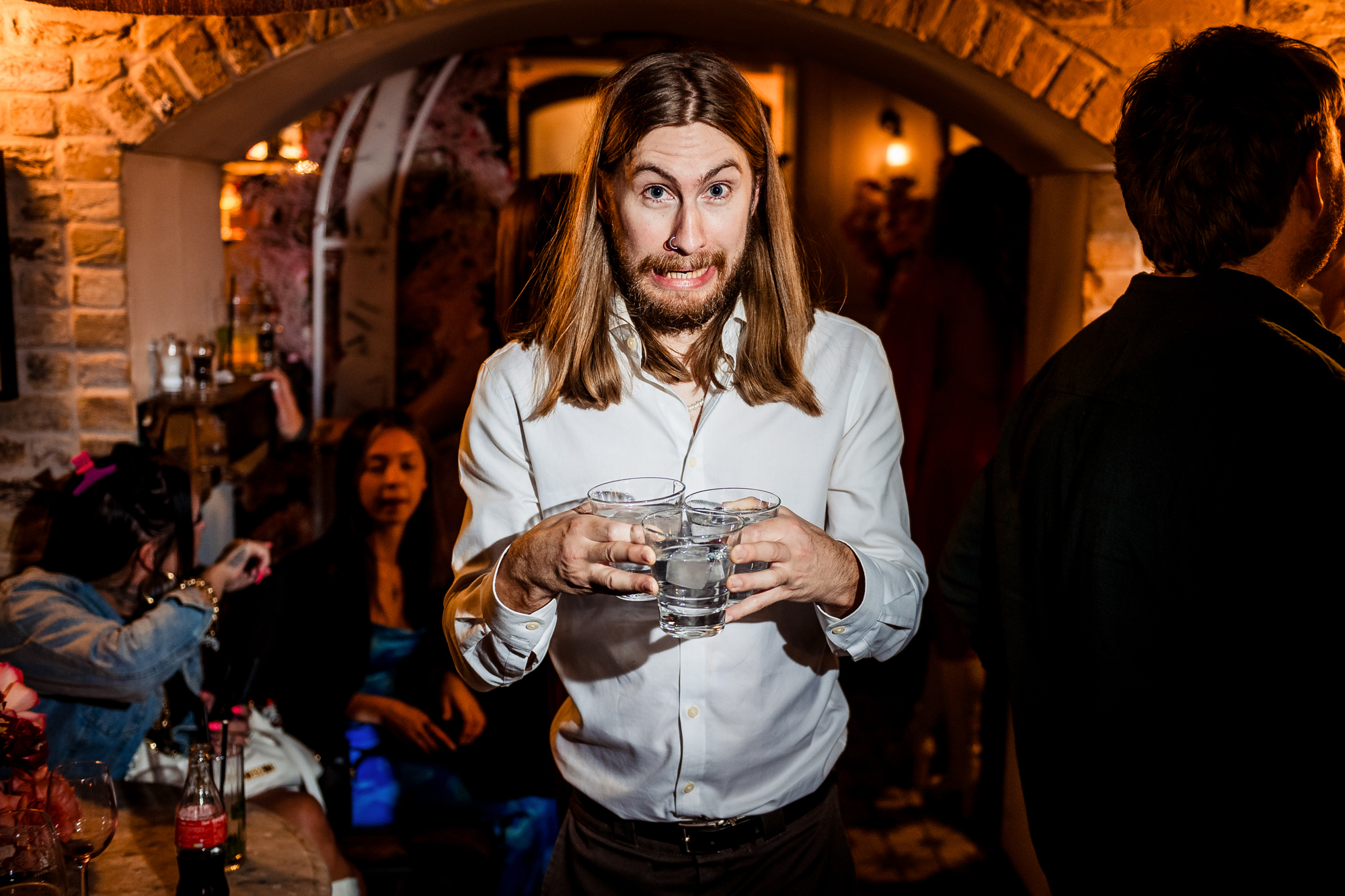 Guest pulls a playful expression while carrying several drinks through the wedding party.