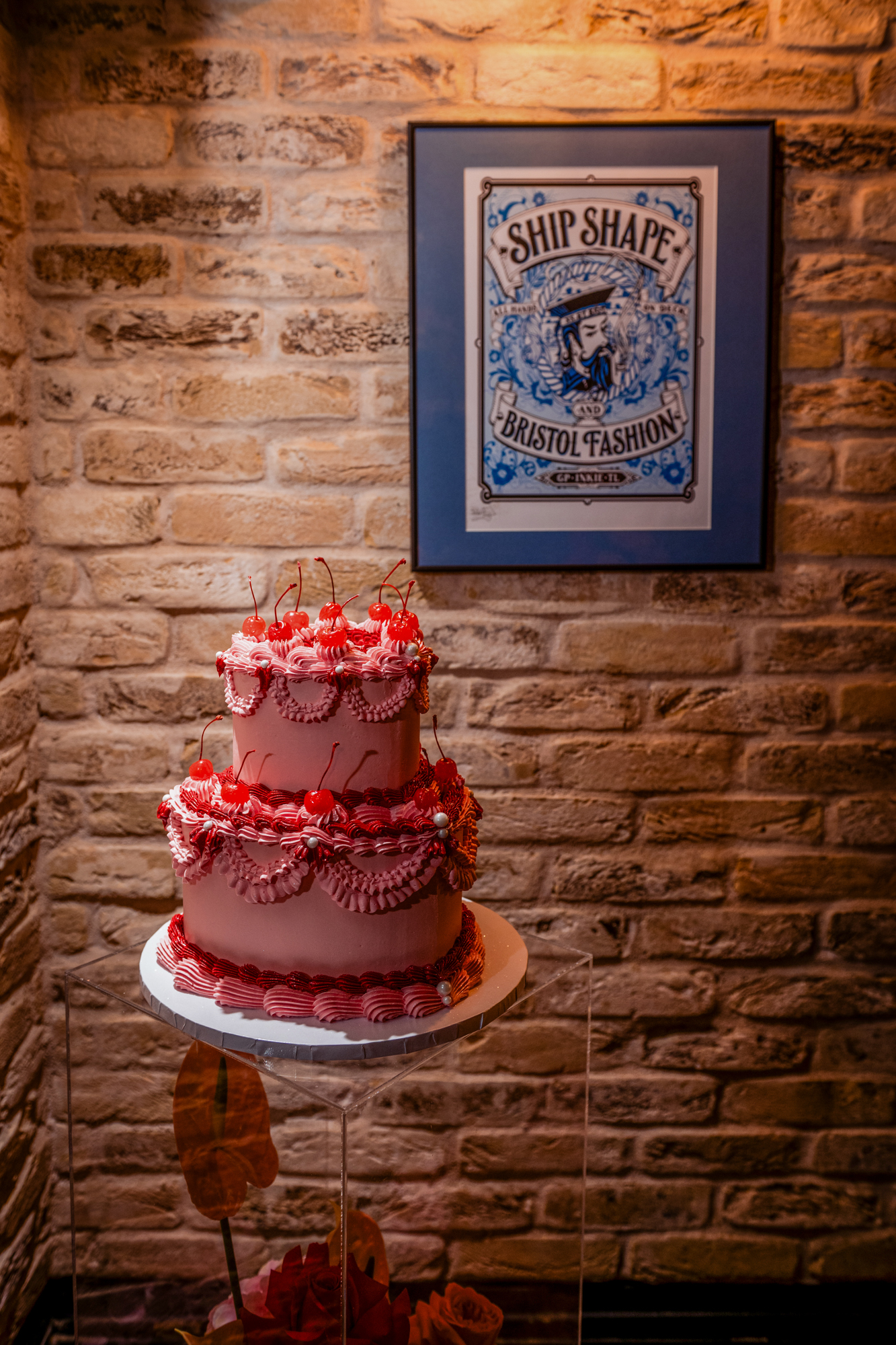 Two-tier pink wedding cake displayed against exposed brick walls in the Playroom at Racks Bristol.