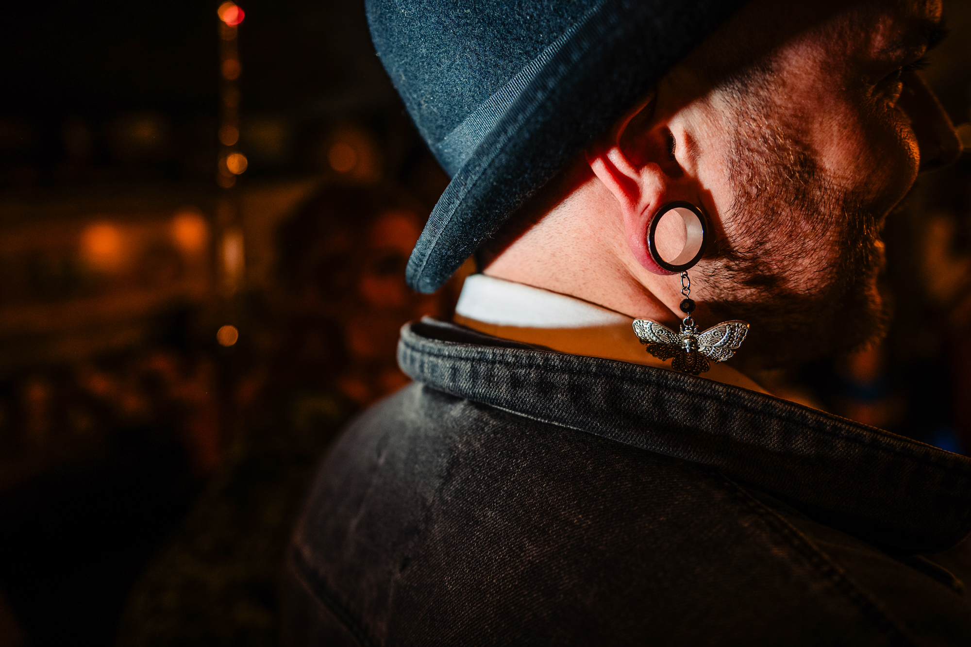 Close-up portrait of a guest in a hat with a butterfly earring and stretched lobe.