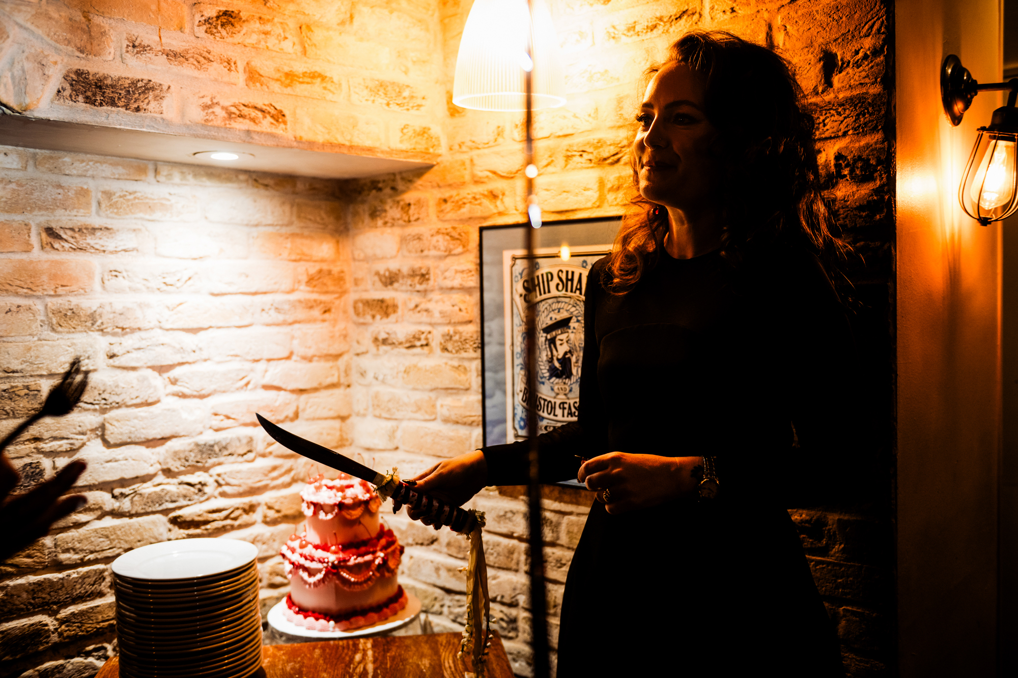 Guest stands in warm light holding the cake knife beside the pink wedding cake.
