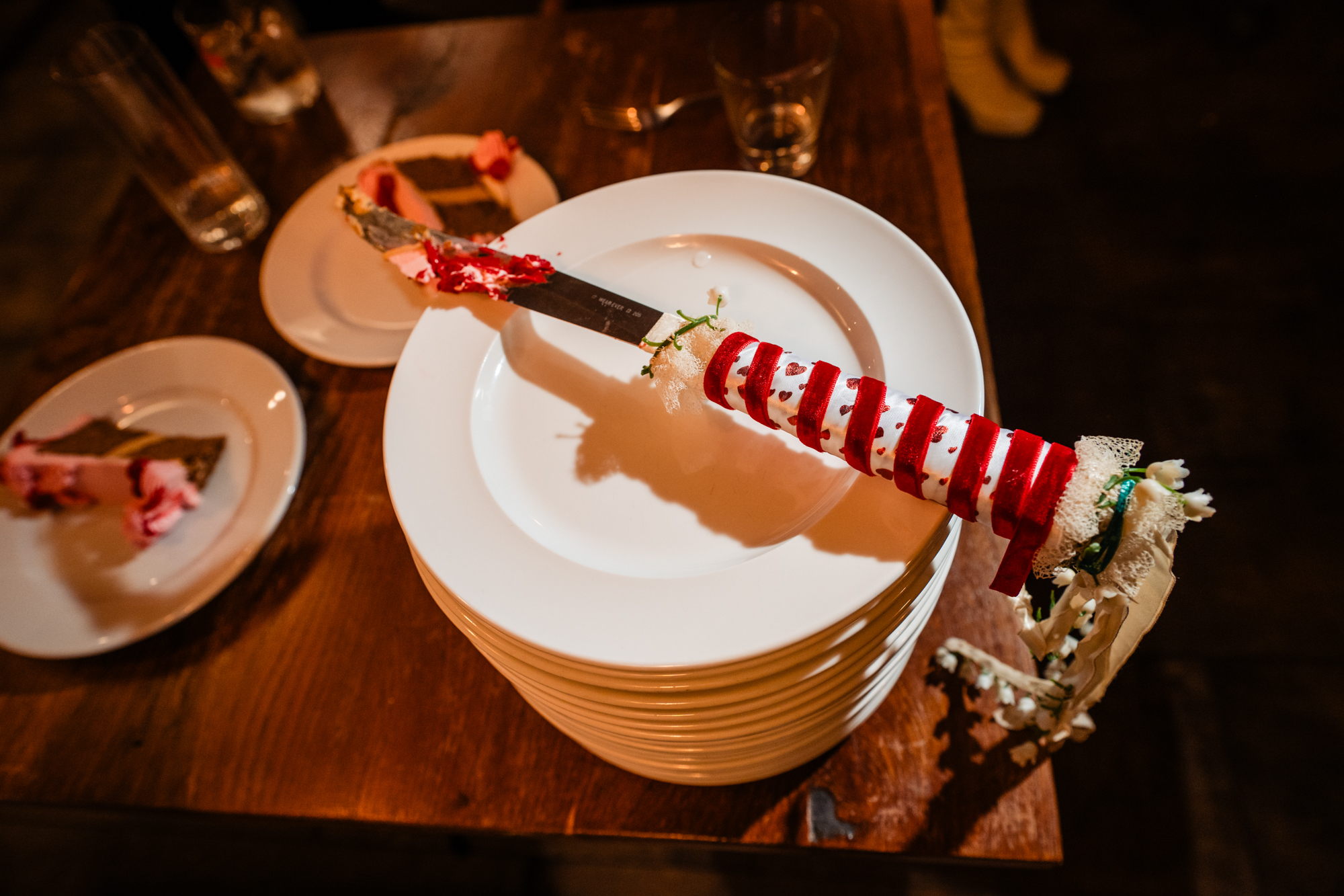Ribbon-wrapped vintage wedding knife resting across stacked plates after the cake cutting.