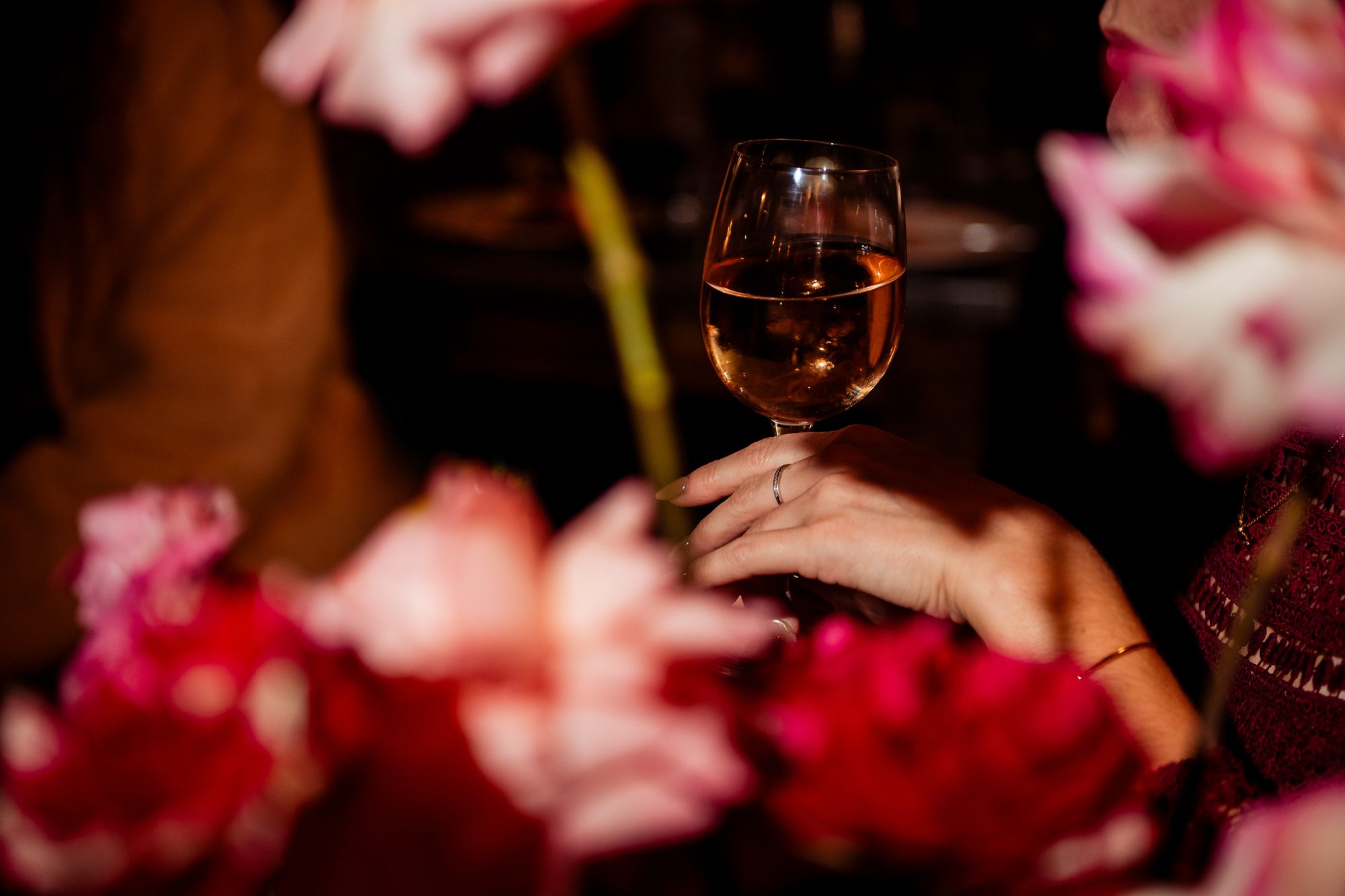 Close-up of a hand holding a wine glass behind blurred pink flowers.