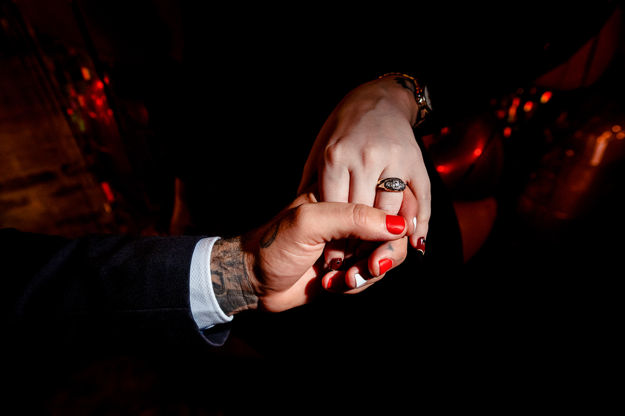 Close-up of tattooed hands holding gently under warm party lighting.