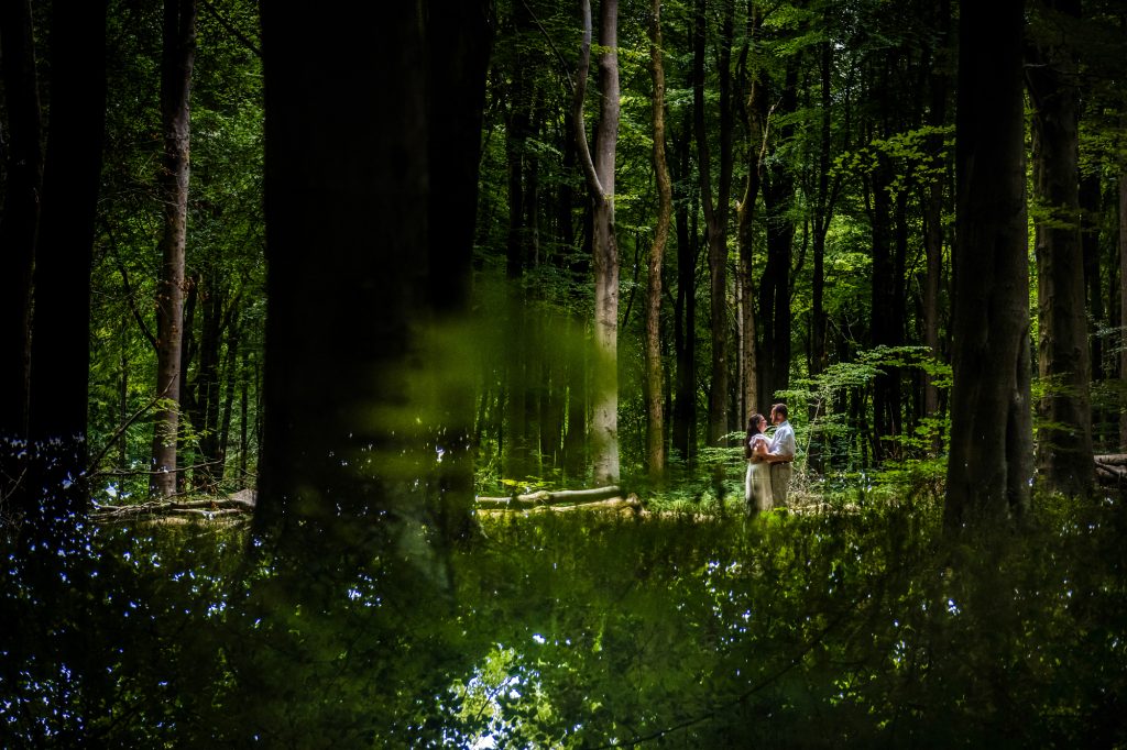 Couple standing together in a forest clearing, surrounded by deep green trees.