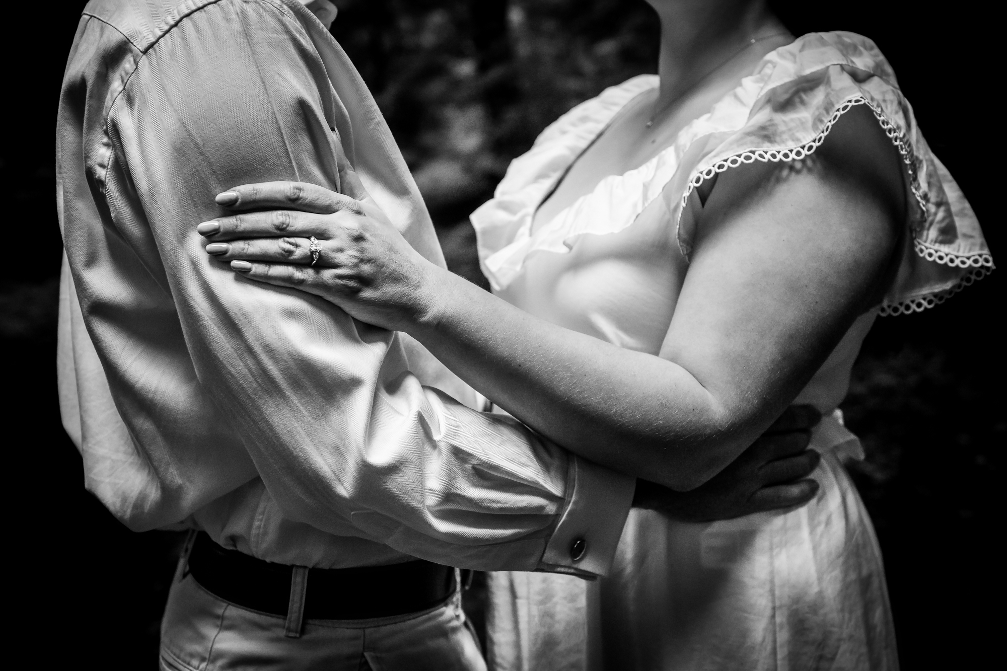 Close-up of an engagement ring as the couple hold each other in black and white.