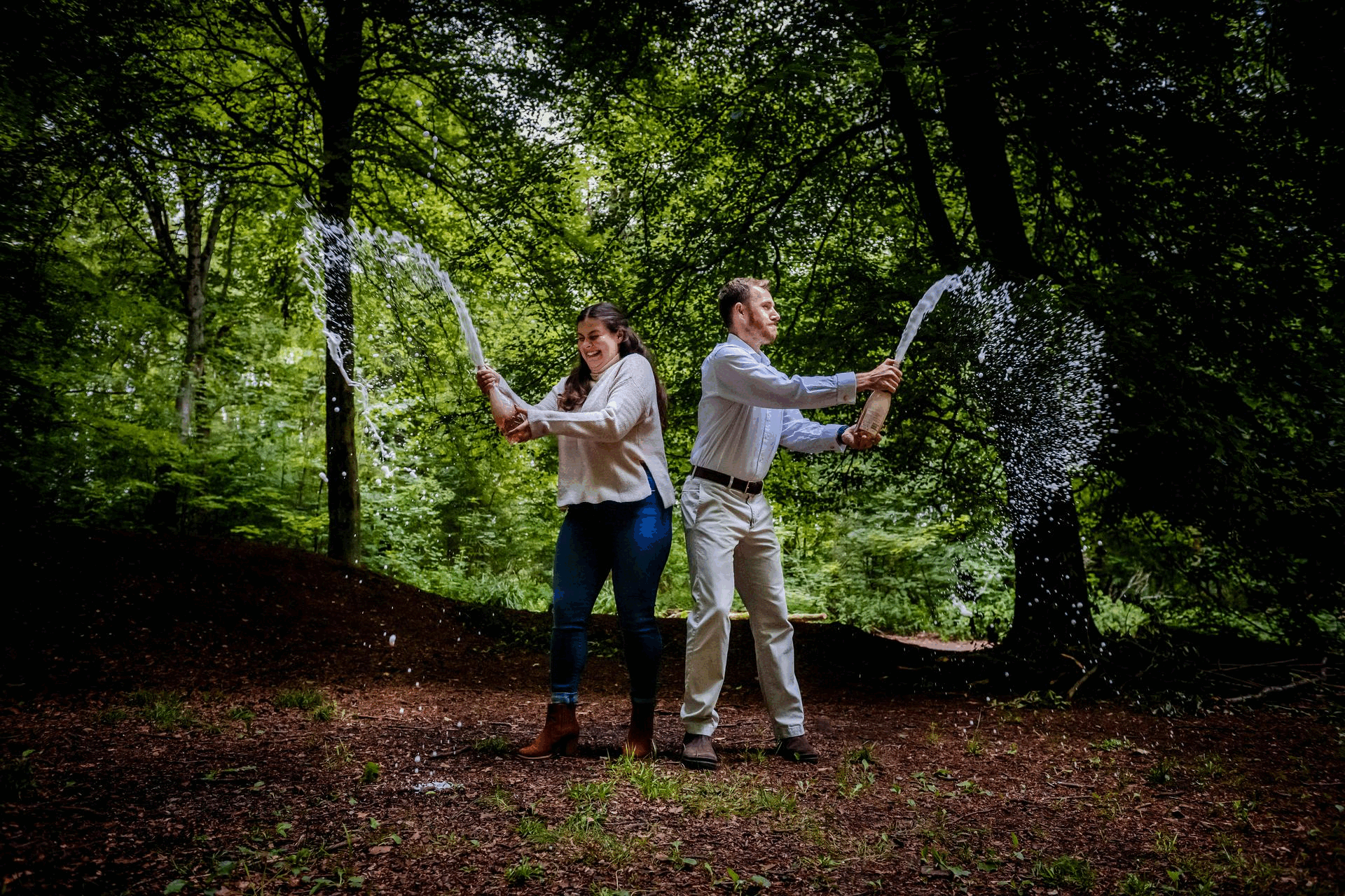 Couple popping champagne in the forest during a playful West Woods engagement session.