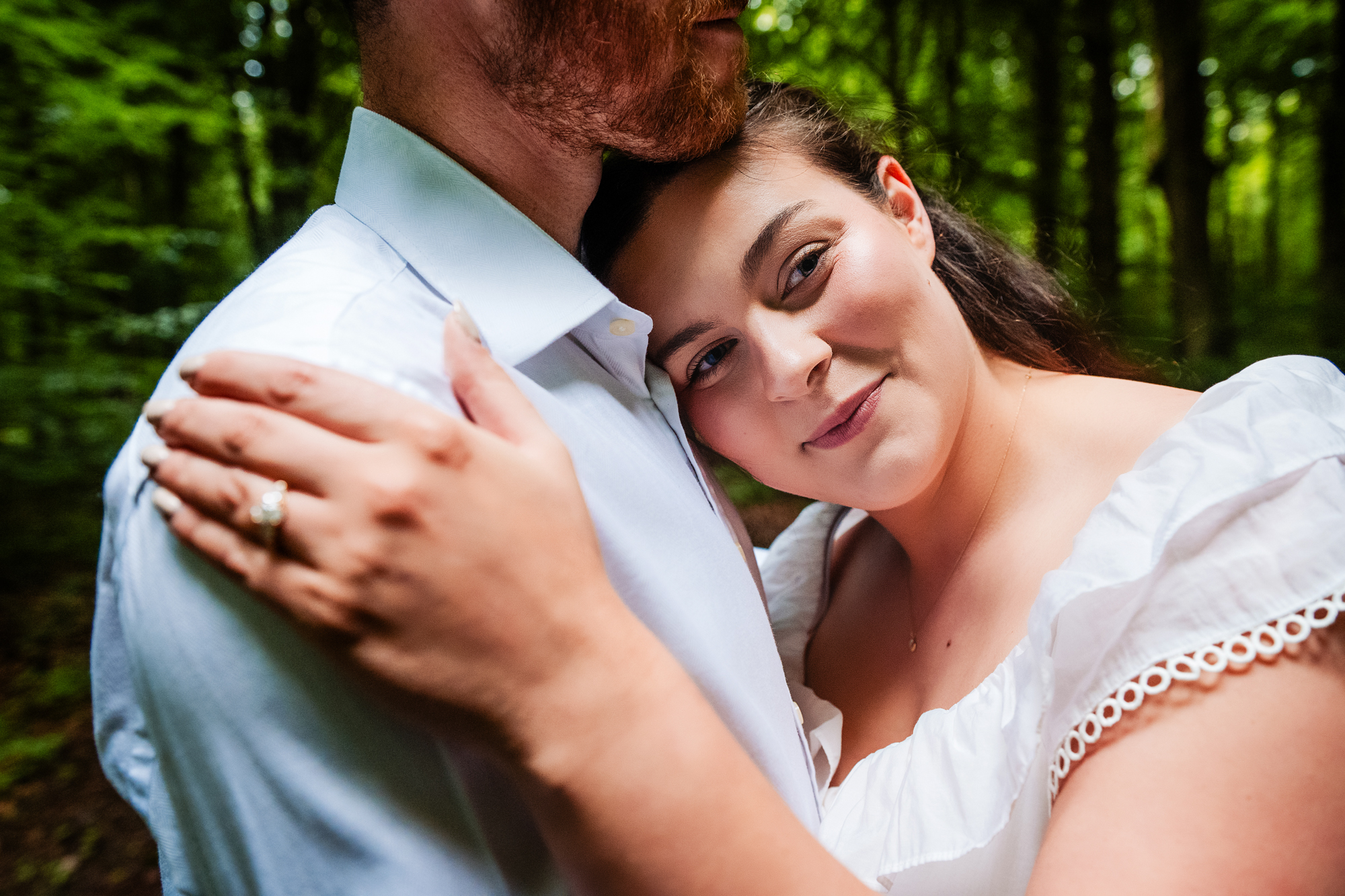 Bride-to-be leaning against her partner and looking at the camera in a forest portrait.