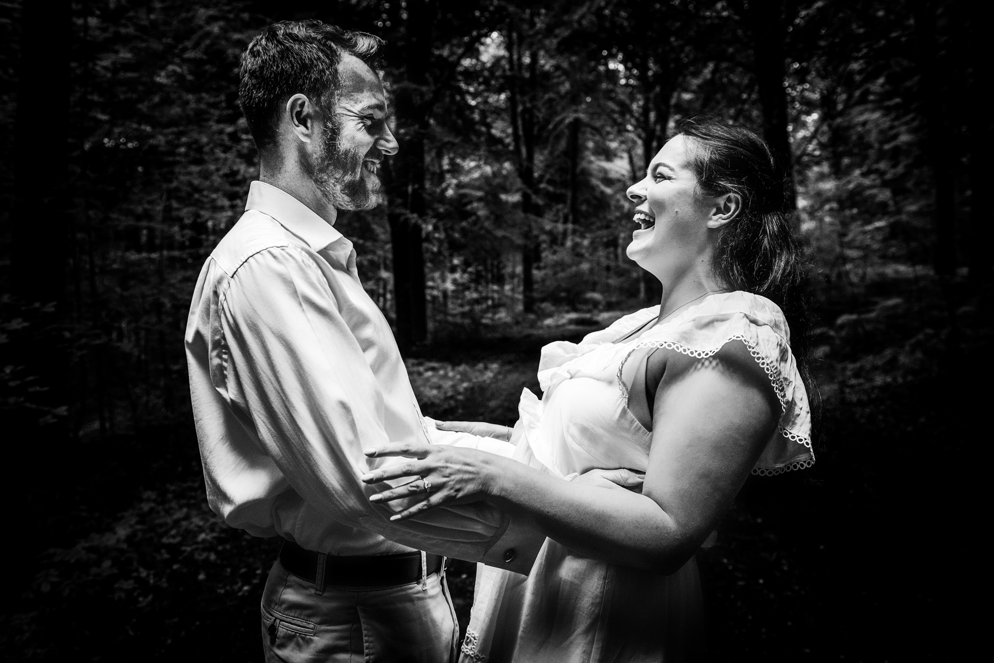Couple laughing together in a dramatic black and white forest engagement portrait.