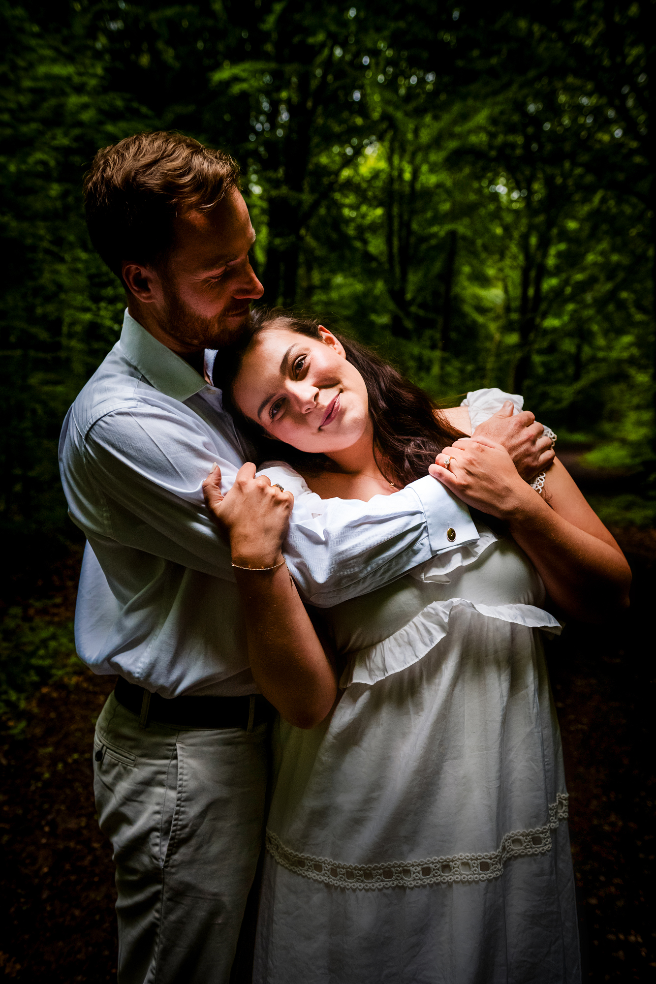 Couple embracing on a woodland path during a moody West Woods engagement shoot.