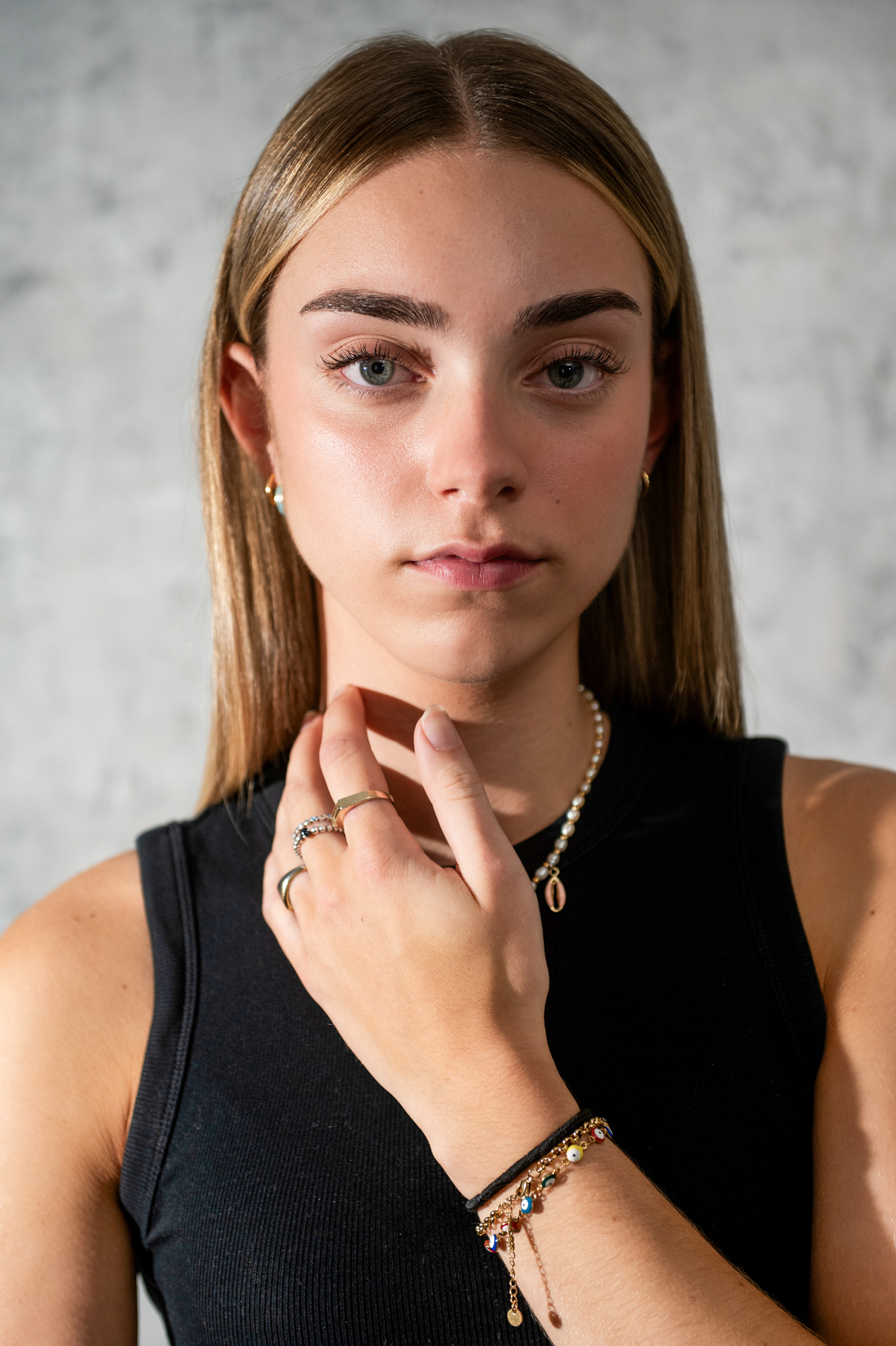 Close-up beauty portrait of young woman with layered necklaces and natural makeup in studio lighting.