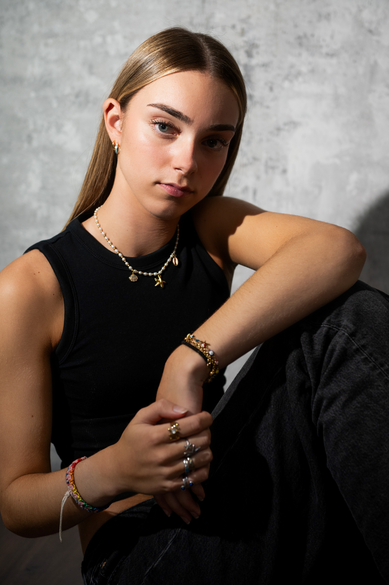 Moody portrait of young woman leaning forward with soft shadow cast on textured studio wall.
