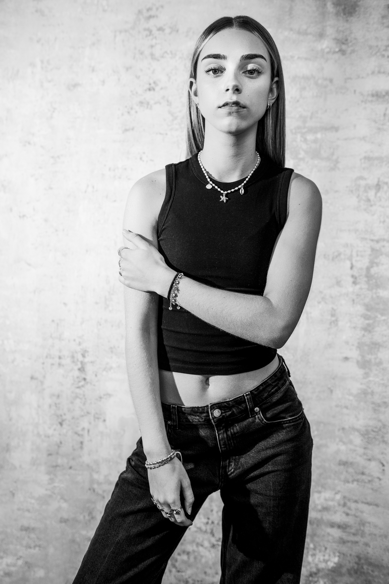 Black and white portrait of young woman standing confidently in minimalist studio with textured backdrop.