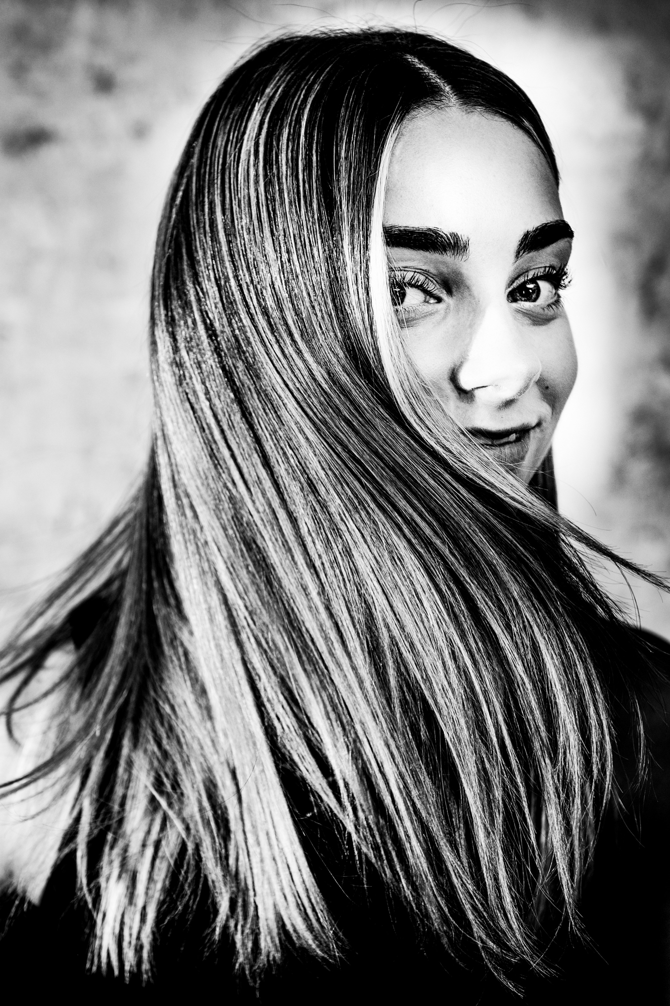 Black and white close-up portrait of young woman with flowing hair covering part of her face.