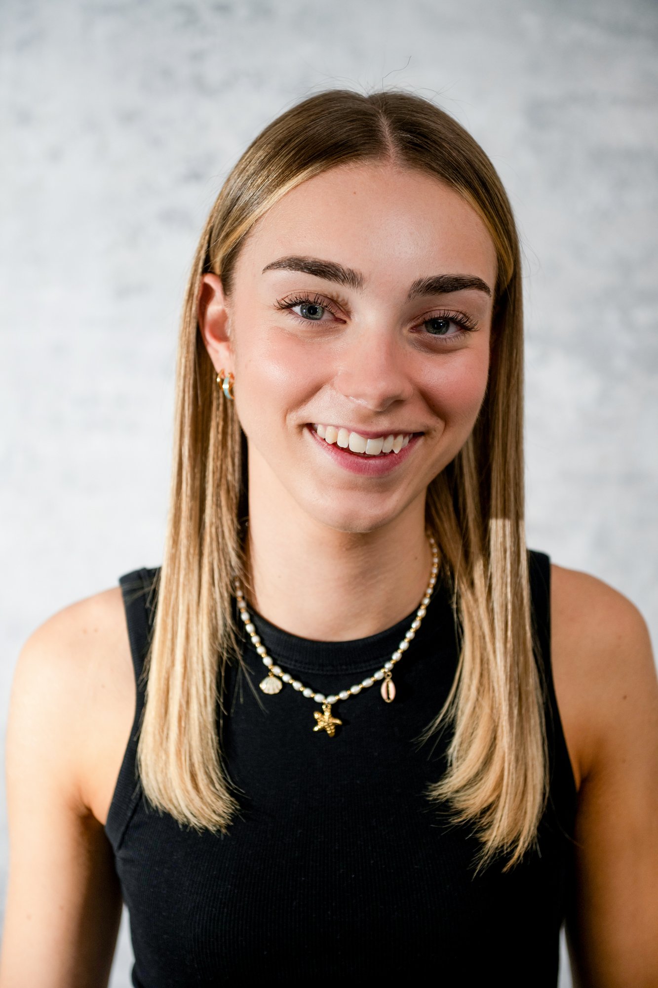 Natural headshot of young woman wearing layered necklaces and subtle makeup in portrait studio.