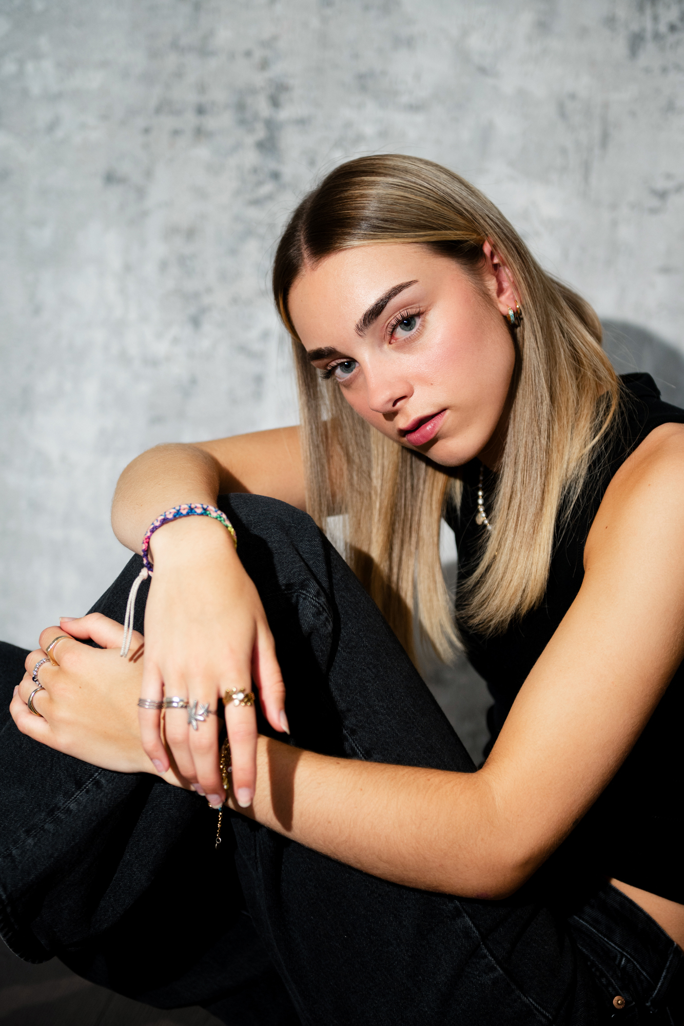 Close-up portrait of young woman with blonde hair leaning on her knee in dramatic studio lighting.