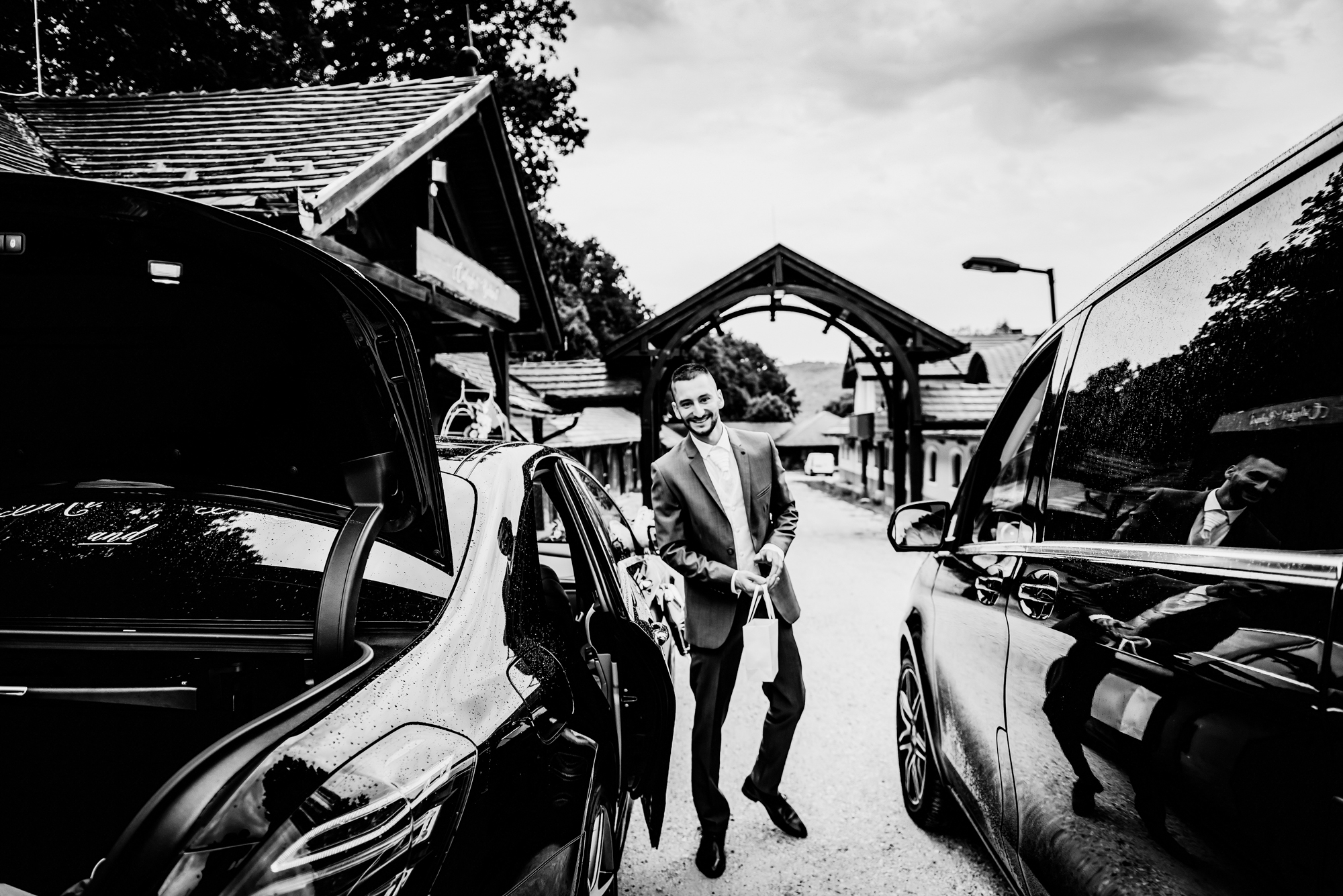 Groom arriving beside wedding cars outside rustic Hungarian wedding venue.