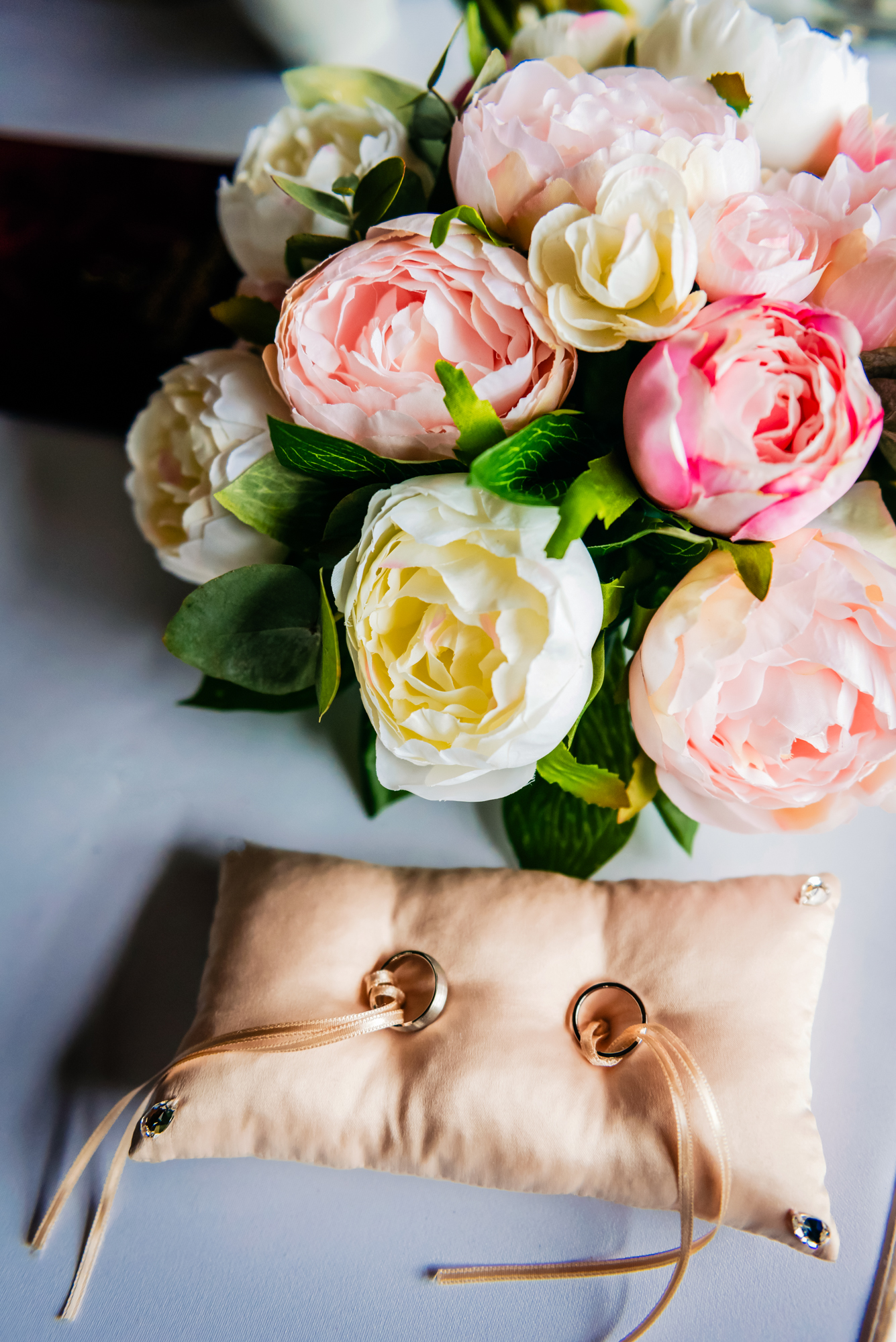 Wedding rings resting on satin ring pillow beside pastel bridal bouquet.