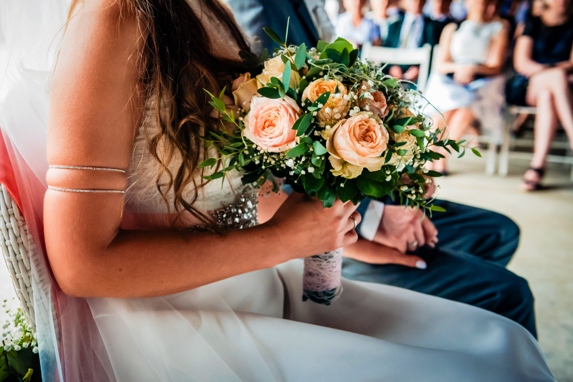 Close-up of bride holding a peach and cream rose bouquet during the ceremony.