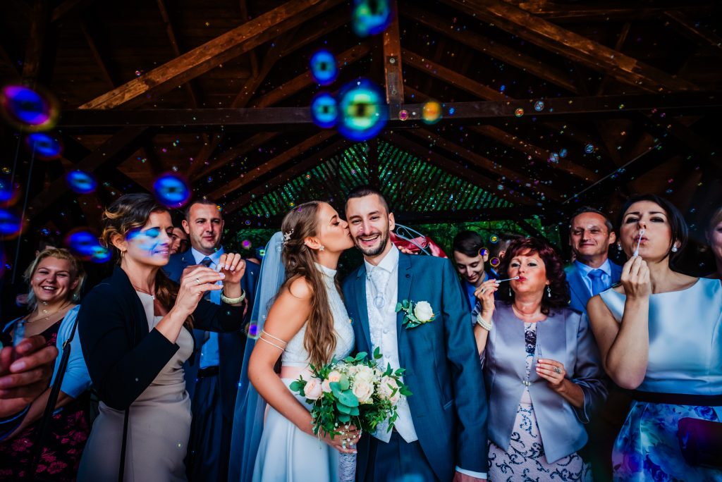 Colourful bubble exit photo of bride and groom surrounded by smiling wedding guests.
