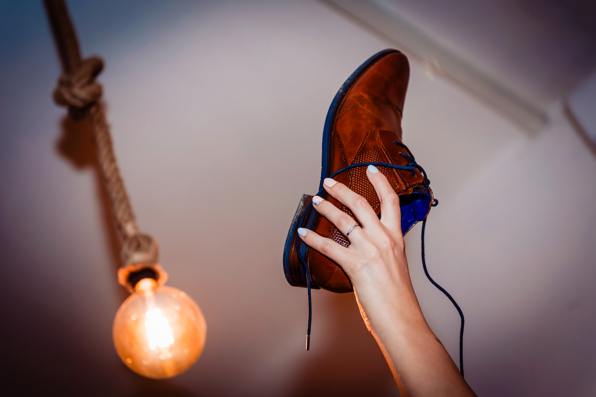 Bride holding up groom’s brown leather shoe during a traditional wedding shoe game at reception.