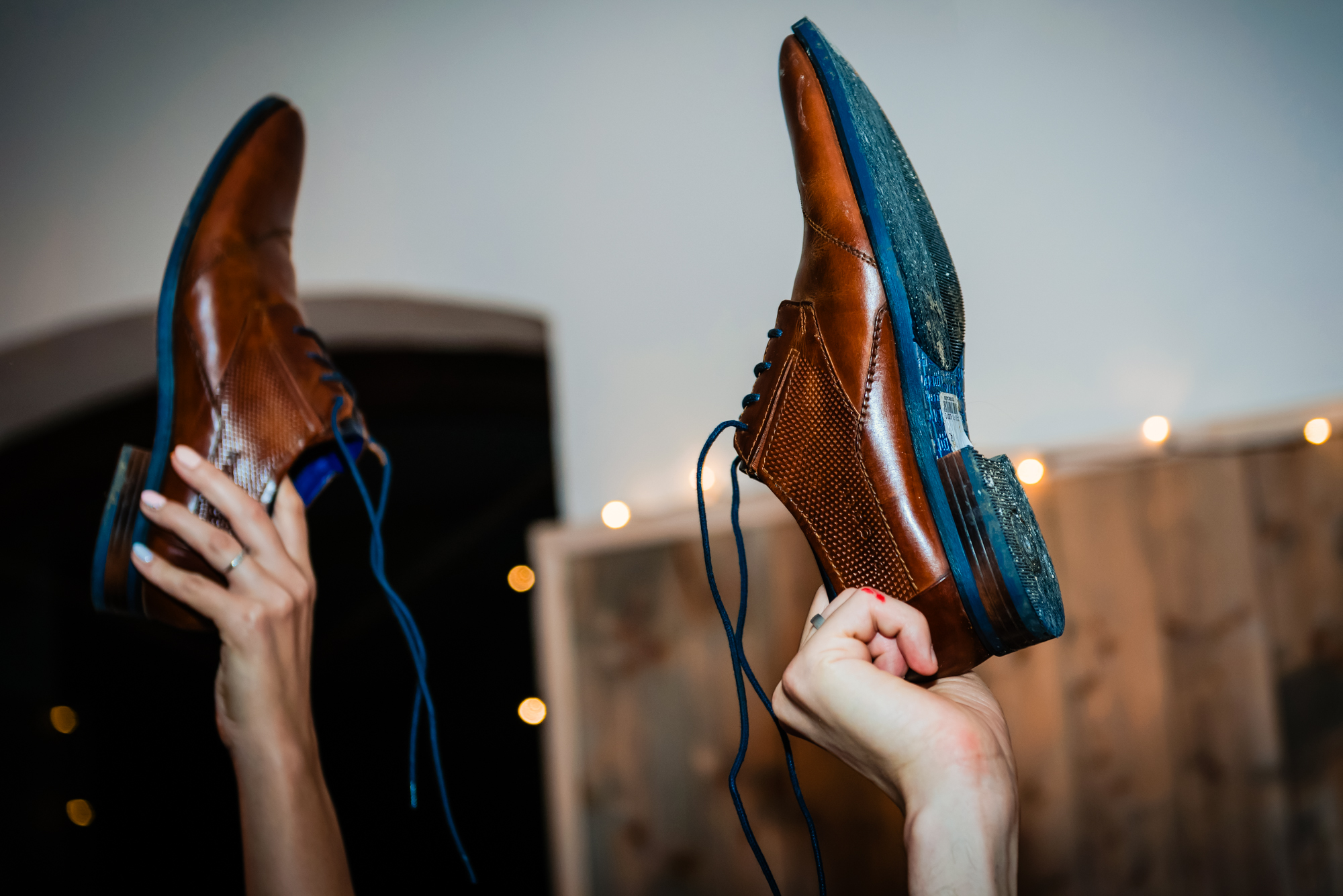 Bride and groom raising brown leather shoes during a lively wedding reception game in Hungary.