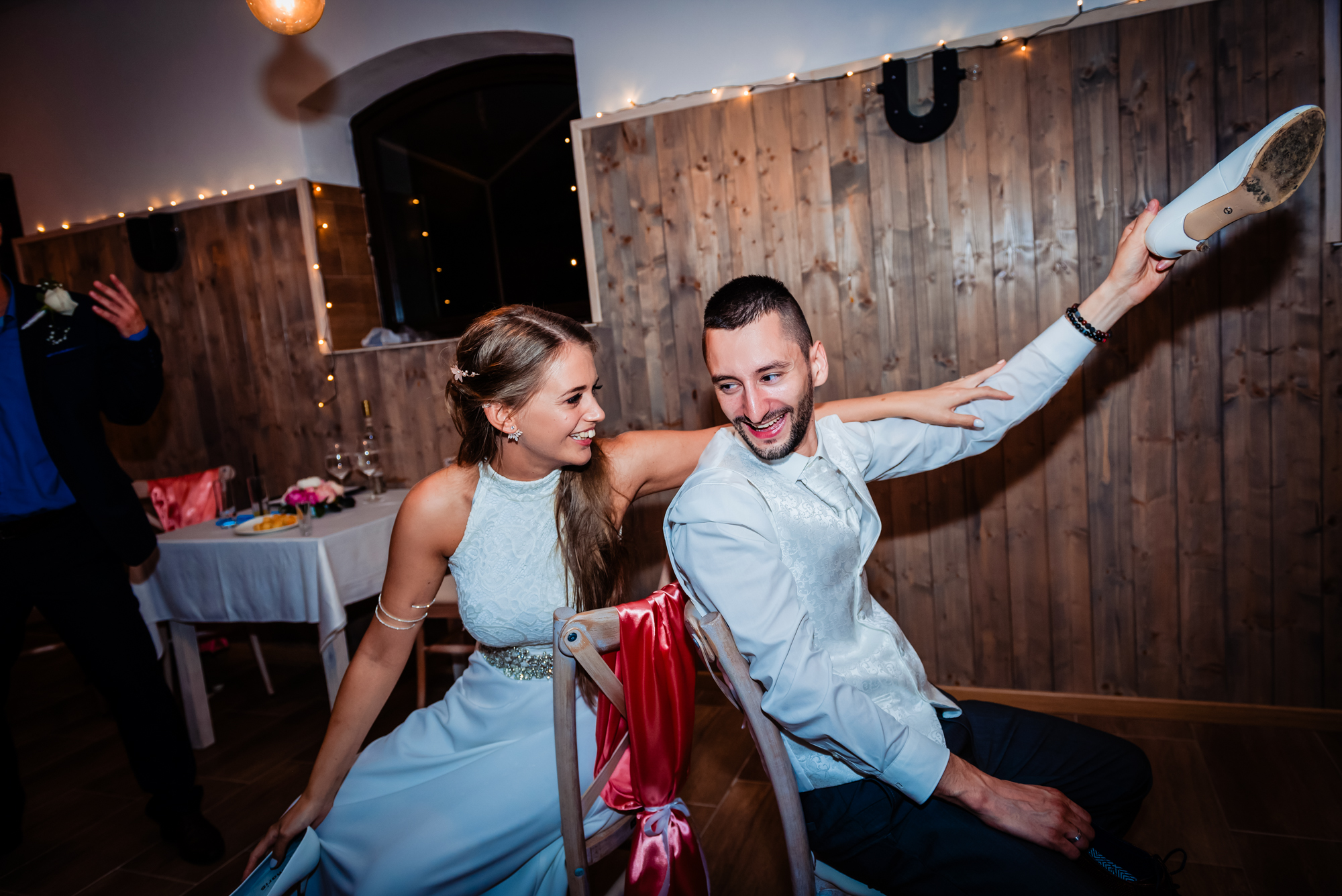 Bride and groom holding shoes above their heads during wedding shoe game at rustic indoor venue.