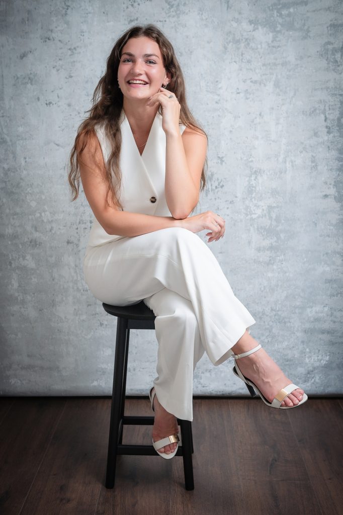 Relaxed studio portrait of smiling woman in white outfit with soft natural posing and grey backdrop.