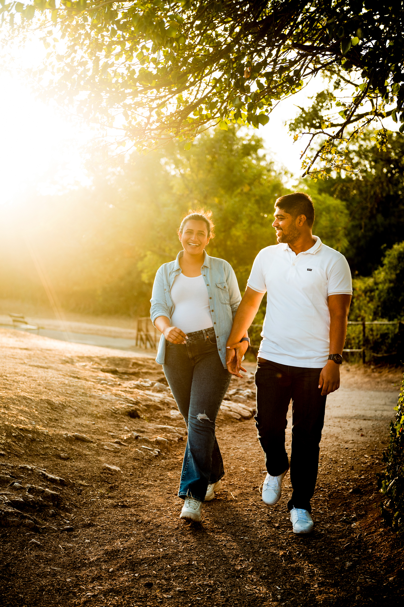 Couple walking together under warm sunset light during relaxed outdoor maternity shoot.