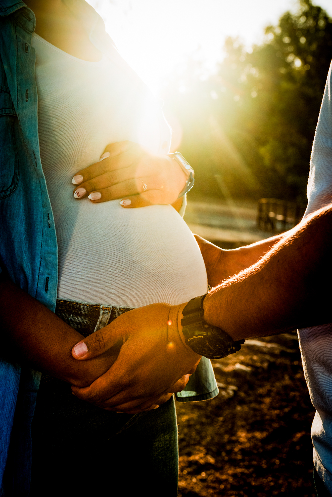 Hands gently holding baby bump in soft golden backlight during outdoor maternity shoot.