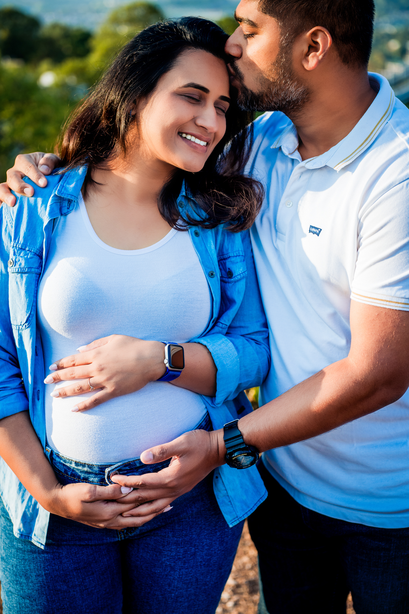 Partner kissing pregnant woman’s head while holding her bump during Bristol maternity session.